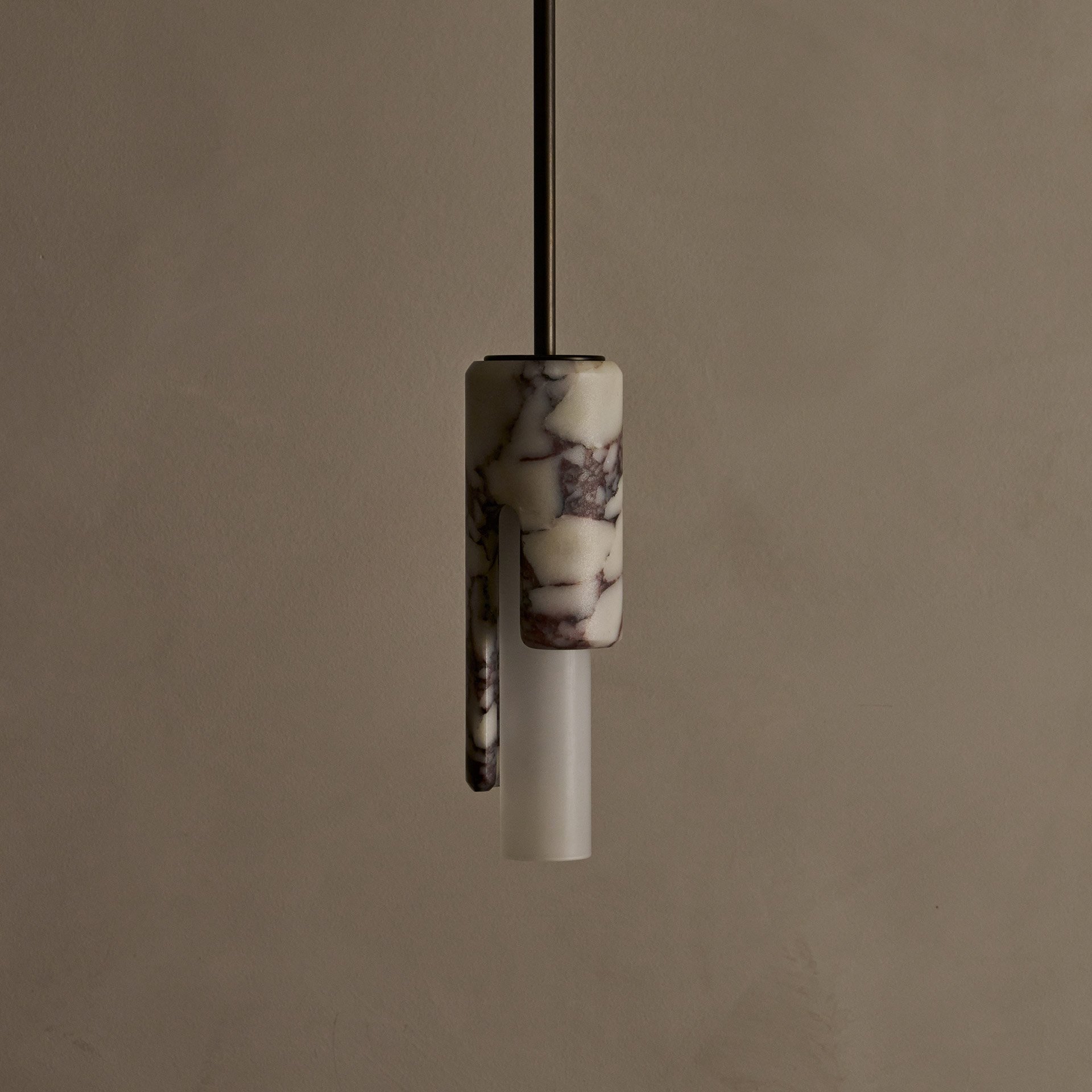 The Dover ceiling pendant features hidden fastening, seamlessly blending stone and glass components. Its cylindrical shade reveals an asymmetric profile from the side.