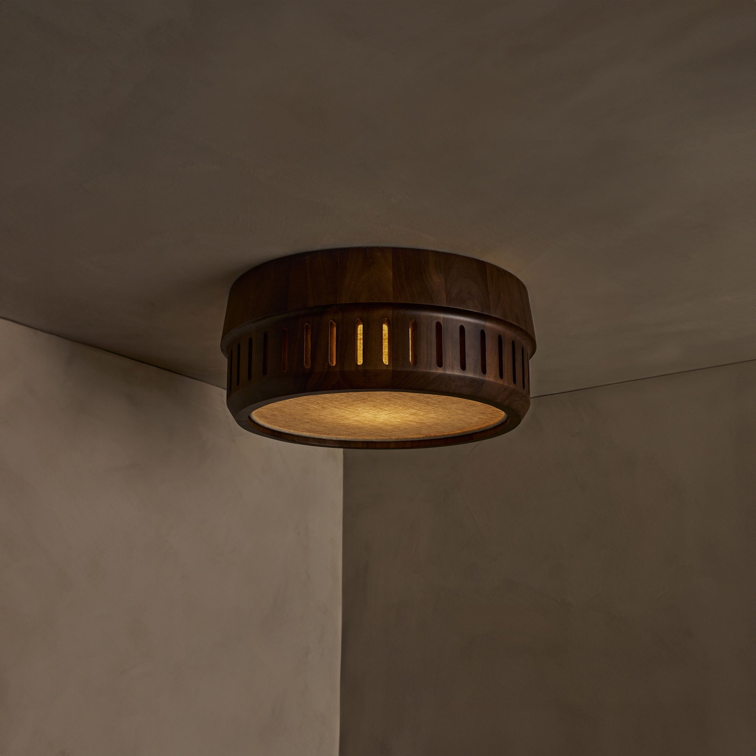 The Adler ceiling mount nests a linen drum shade within a solid wood exterior, offering functional downward illumination. Notches in the wood allow glimpses of the fabric shade within.
