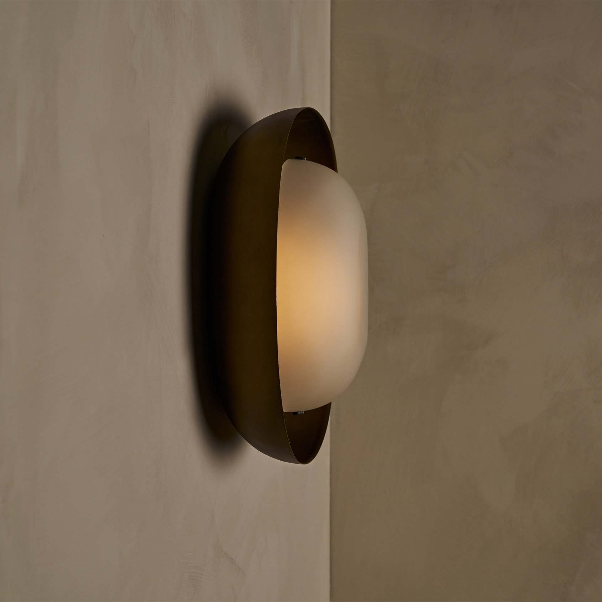 The Dormus Sconce, featuring a brass exterior enclosing an inverted glass shade of matching shape, showcasing a striking interplay of negative space within the elegant design.