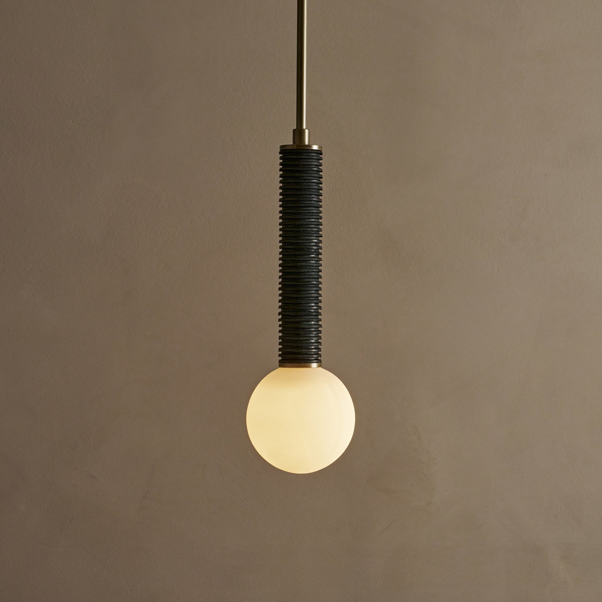 The Pell pendant lamp features a solid body crafted from stacked leather hide disks, showcasing the natural imperfections of the material's edge. A frosted glass sphere hangs at the bottom.