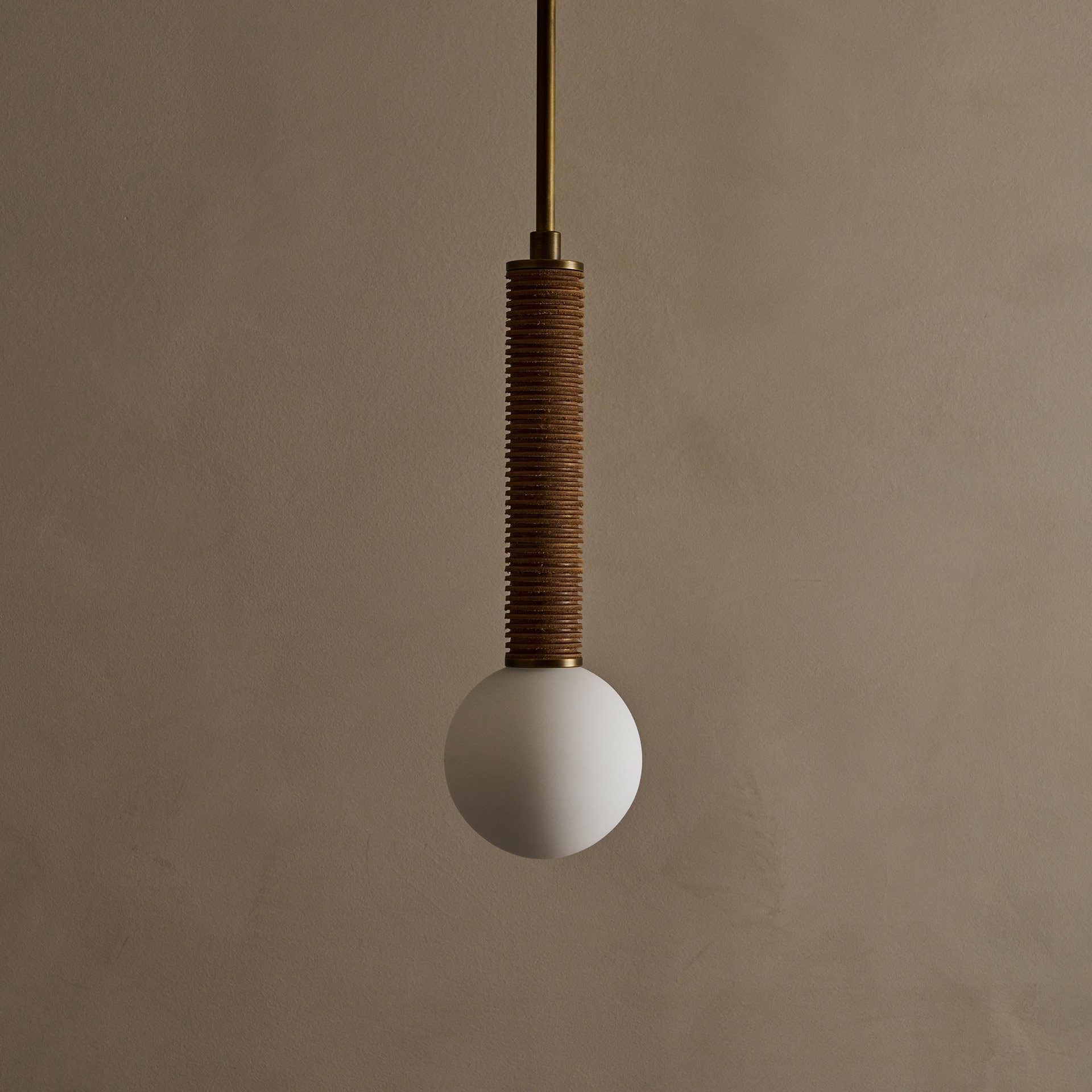 The Pell pendant lamp features a solid body crafted from stacked leather hide disks, showcasing the natural imperfections of the material's edge. A frosted glass sphere hangs at the bottom.