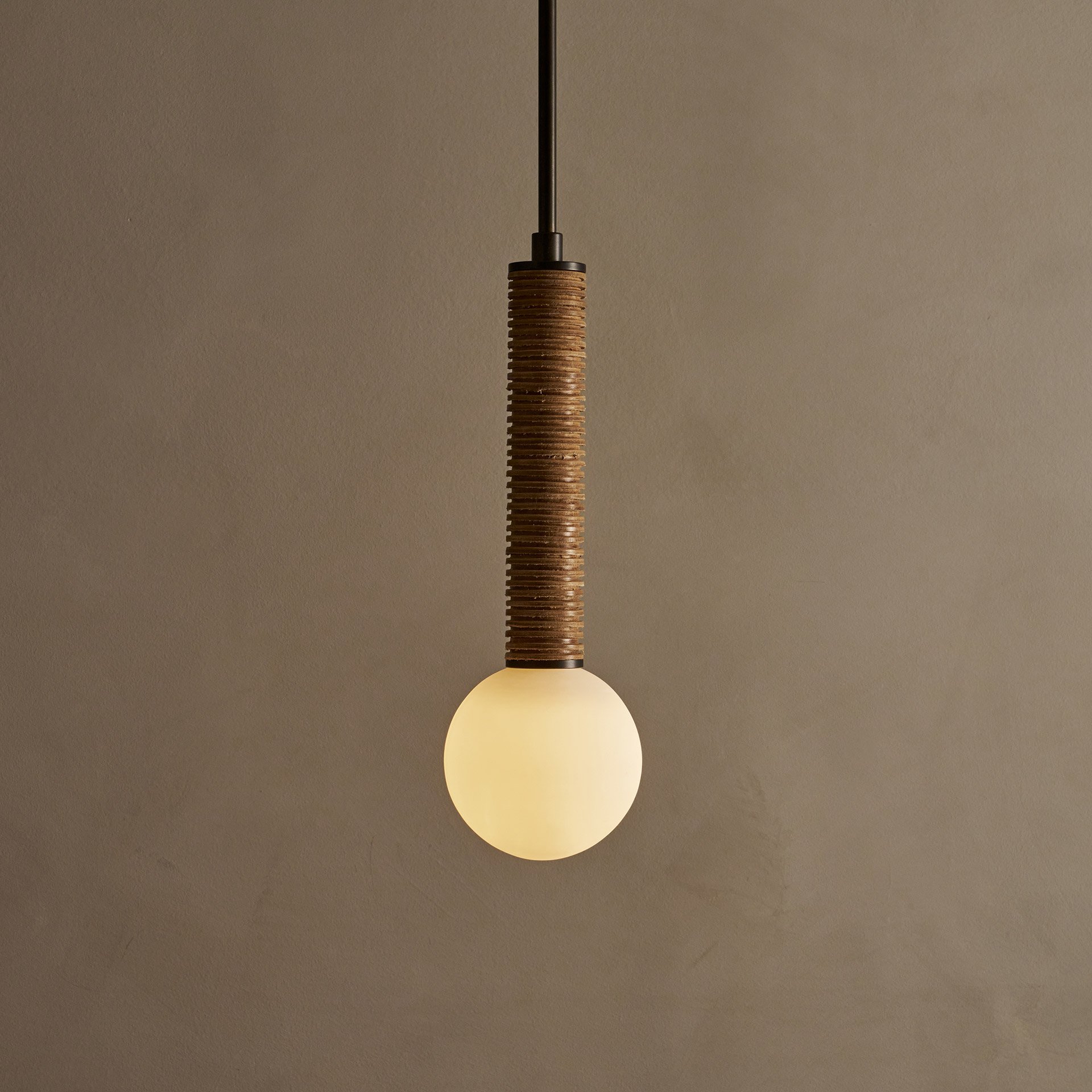The Pell pendant lamp features a solid body crafted from stacked leather hide disks, showcasing the natural imperfections of the material's edge. A frosted glass sphere hangs at the bottom.