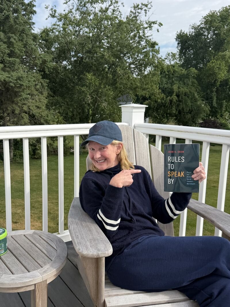 Amanda Haverstick sitting on her deck hold the book Rules to Speak by, by John Snow