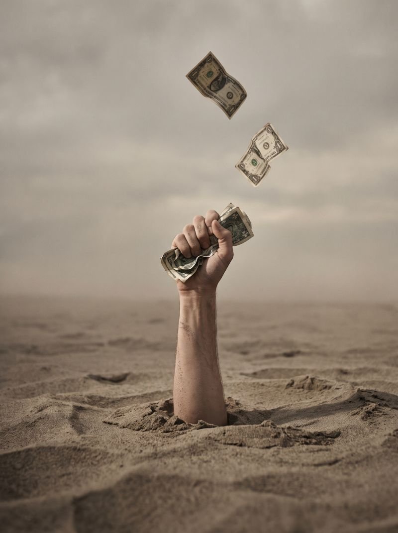 hand coming out the the sand holding money