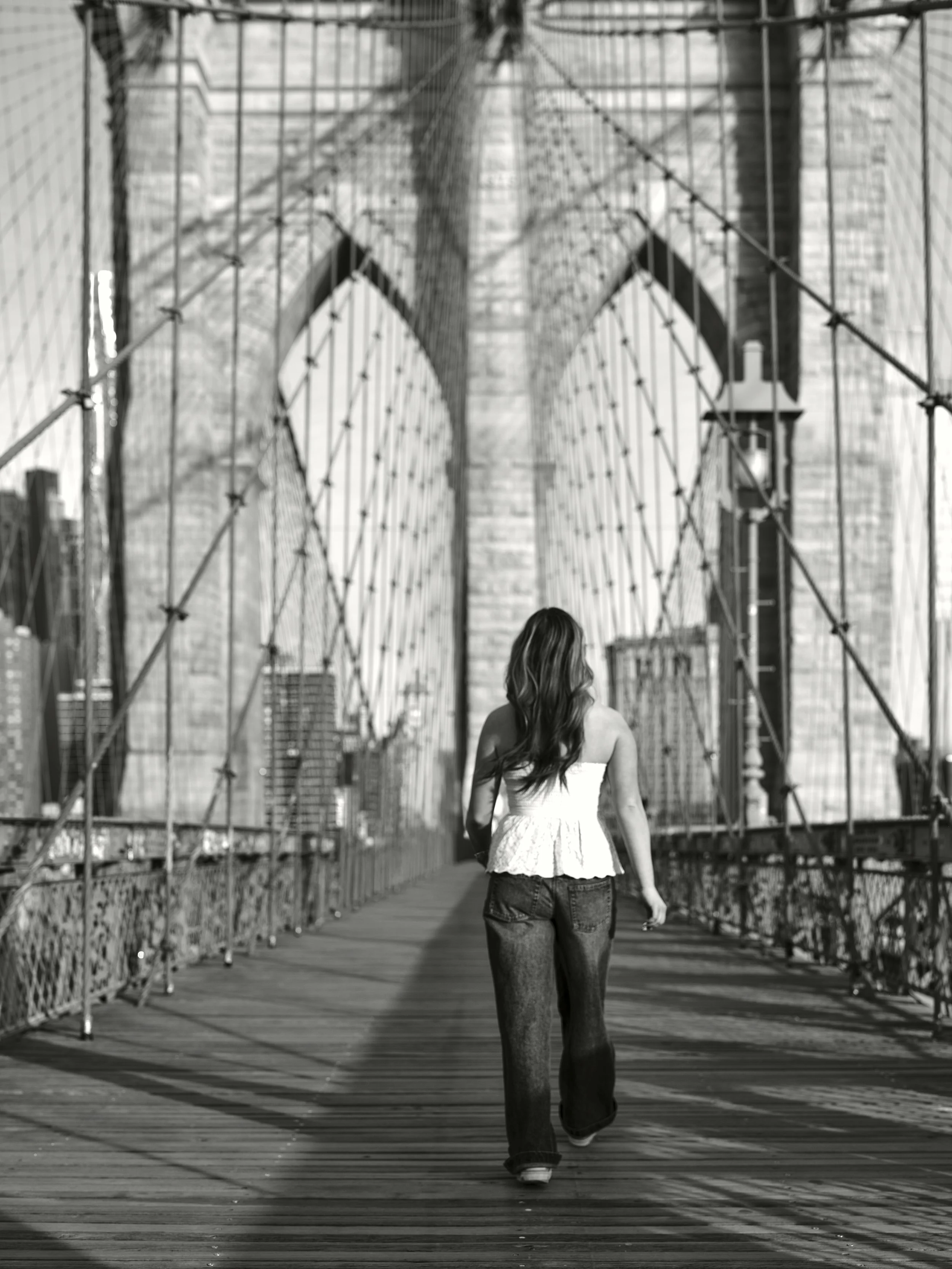 Black and White image of a woman walking away on Brooklyn Bridge NYC