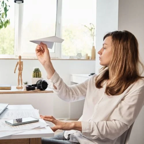 A person about to fly a paper airplane while sitting at her desk.