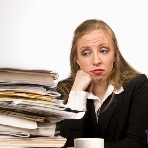 A person sitting with a pile of folders and books in front of her.