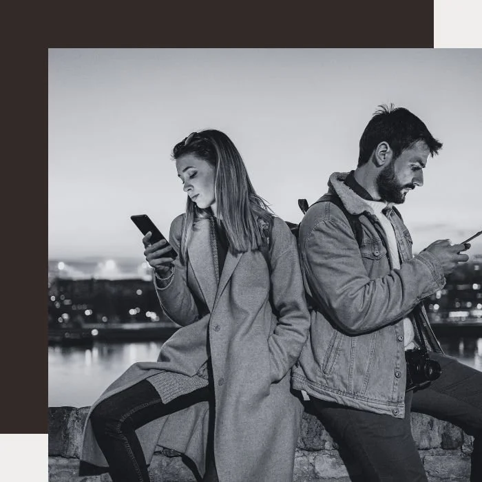 A couple wearing backpacks and looking at their phones