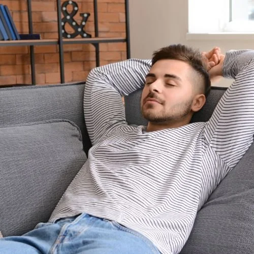 A person resting on a sofa. His eyes are closed.