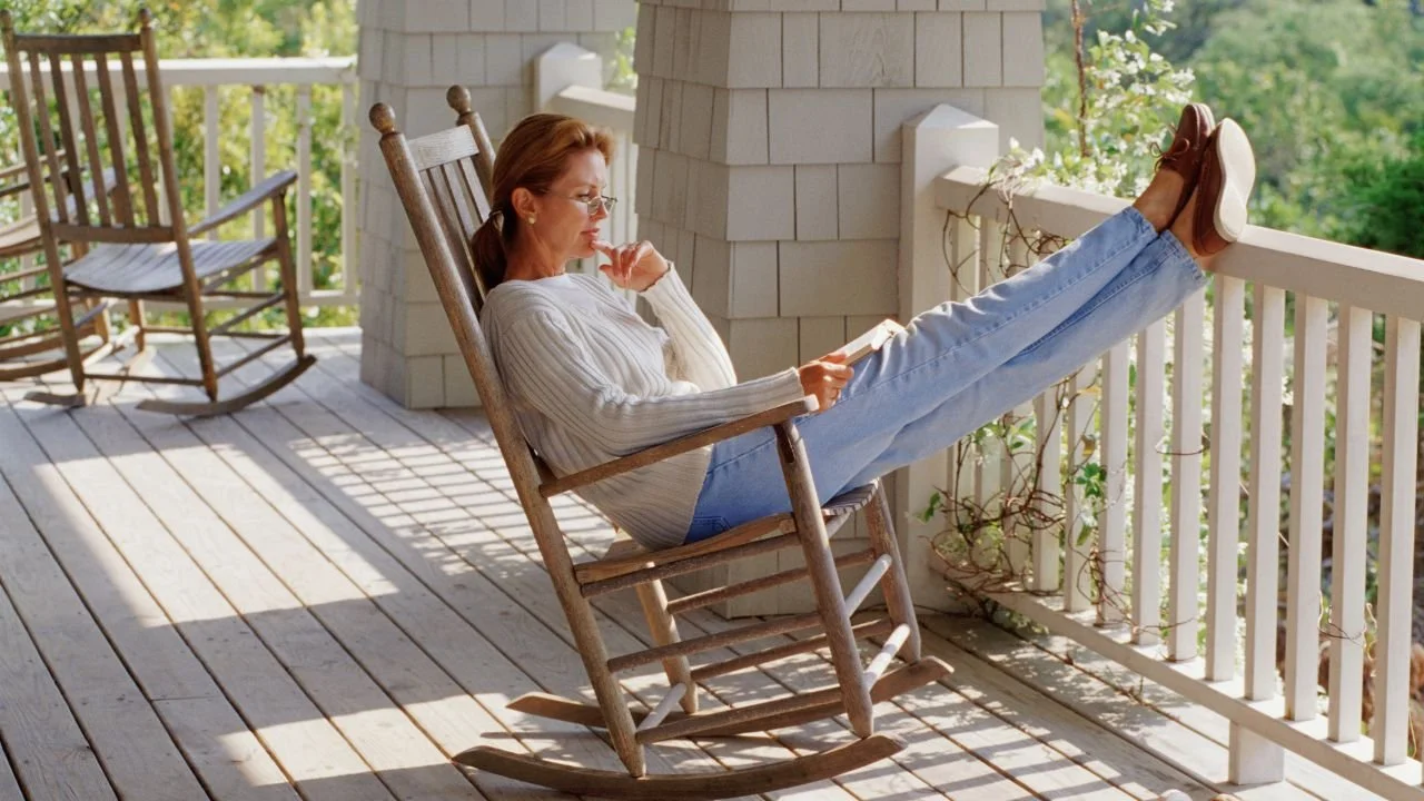 A woman relaxing while reading a book on a porch.