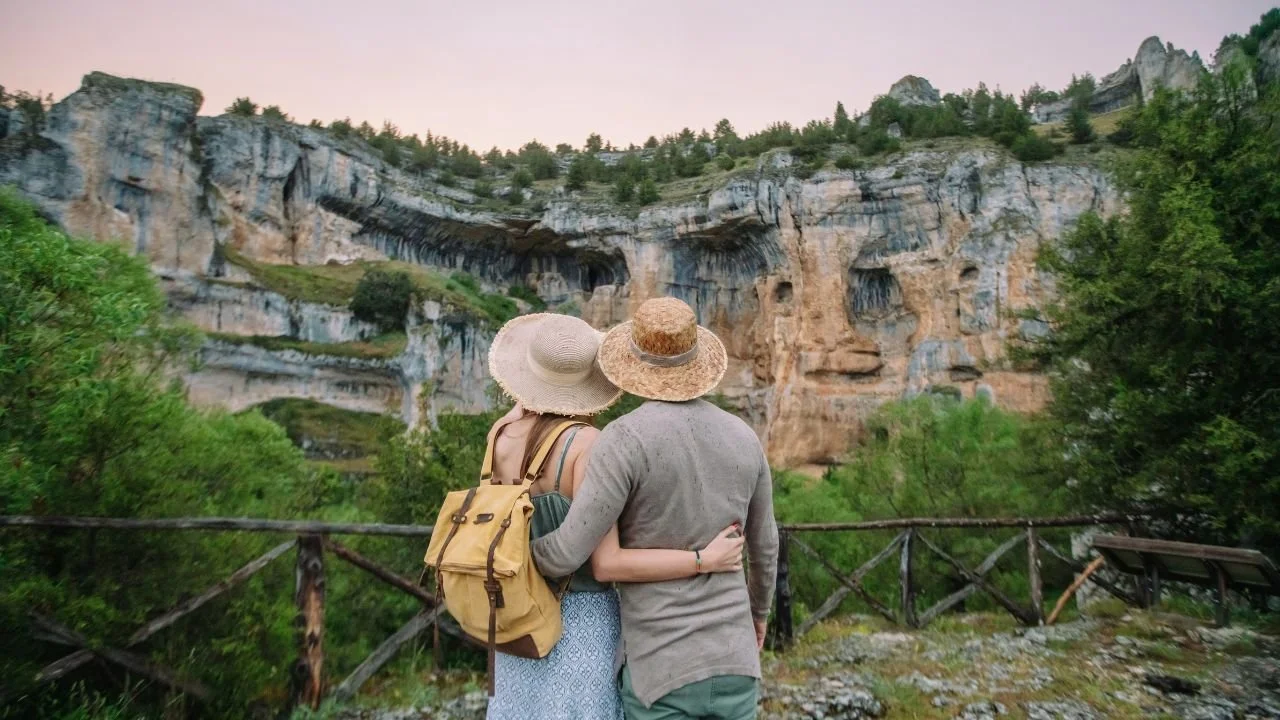 A couple of tourists looking at a cliffside full of caves.