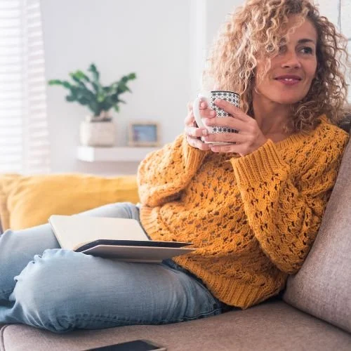A woman dressed in a sweater and jeans. She is drinking coffee.
