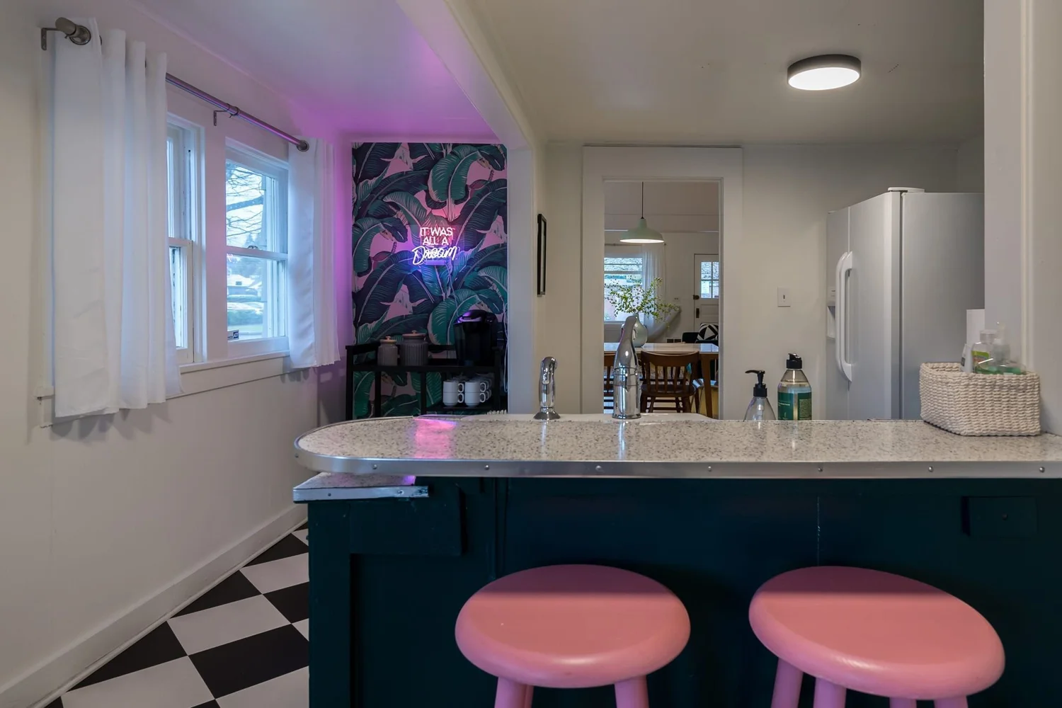 Pink stools at the teal kitchen island under a neon sign