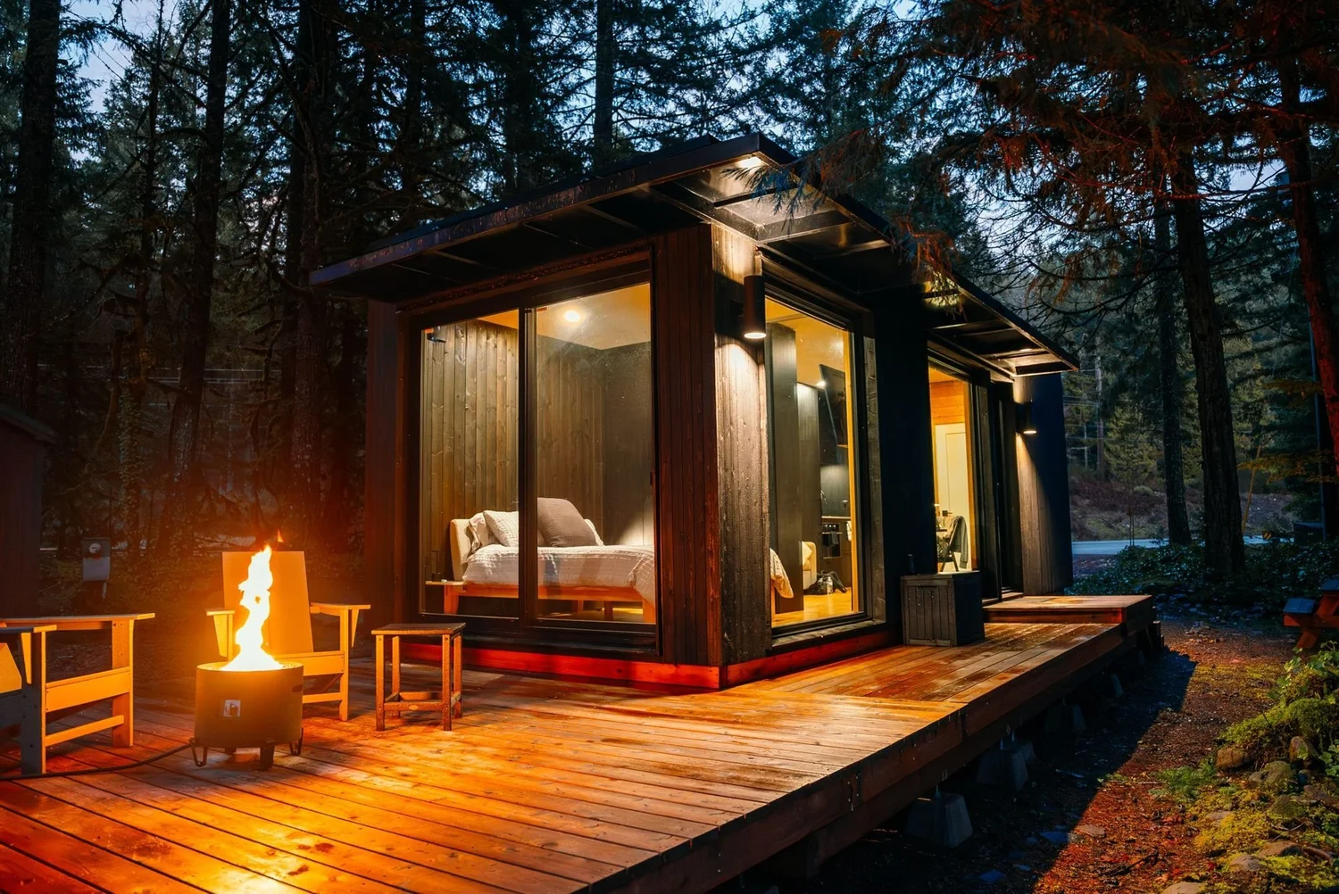The tiny home glowing at dusk with the fire pit lit on the cedar deck