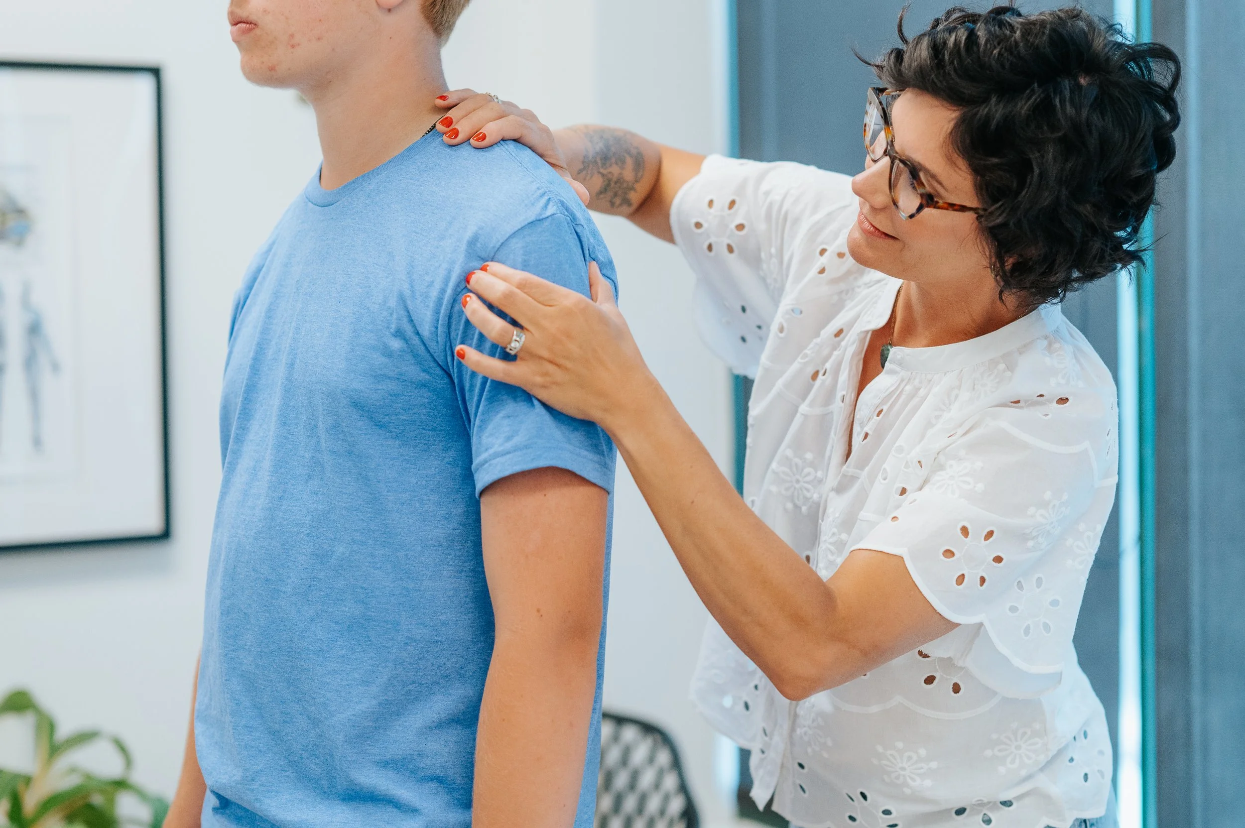 A person receiving physical therapy or stretching exercise from a therapist on a red yoga mat, with a wooden floor in the background.