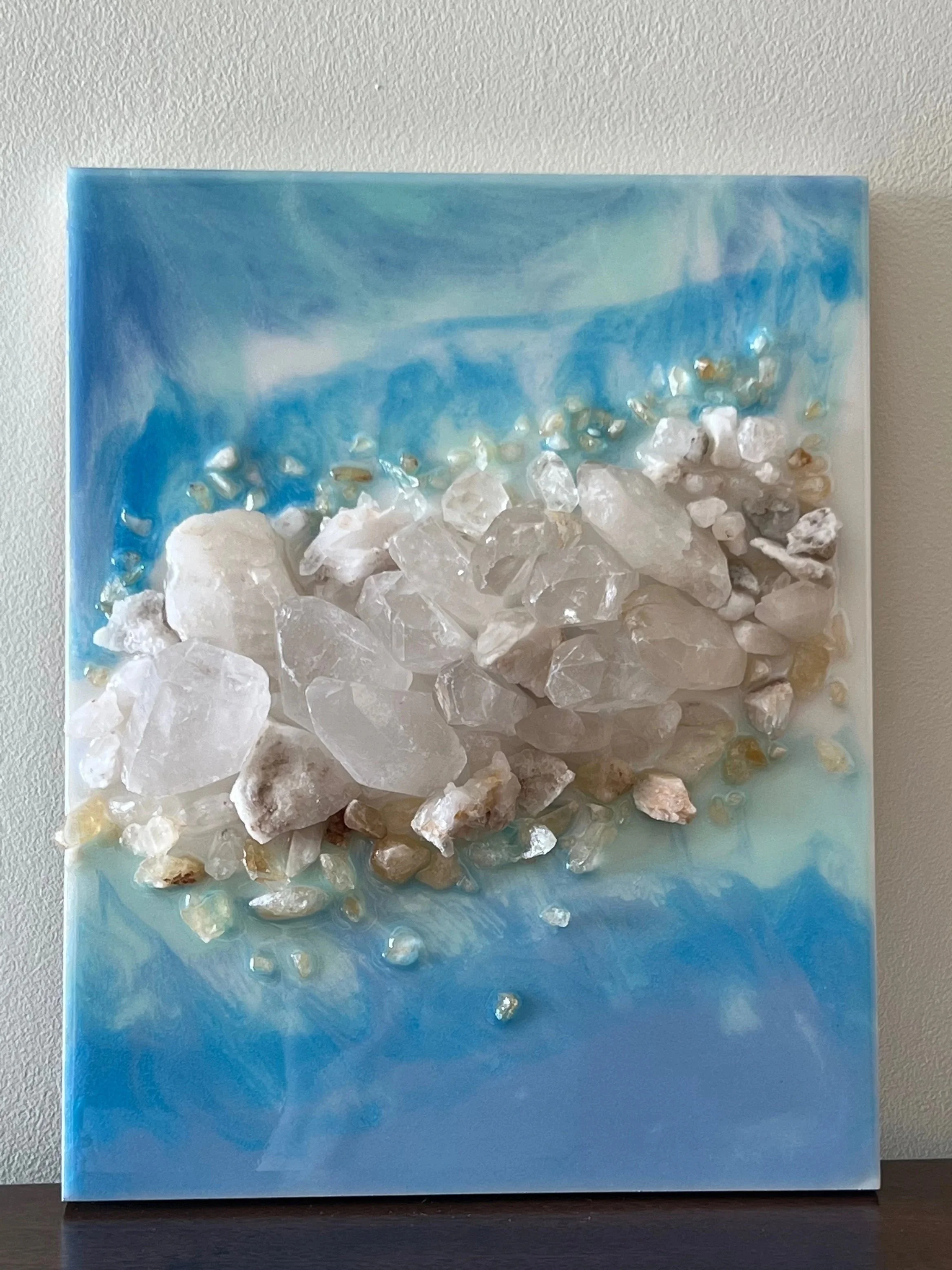 Mixed media artwork featuring white rocks and small beads on a blue and white marbled background.