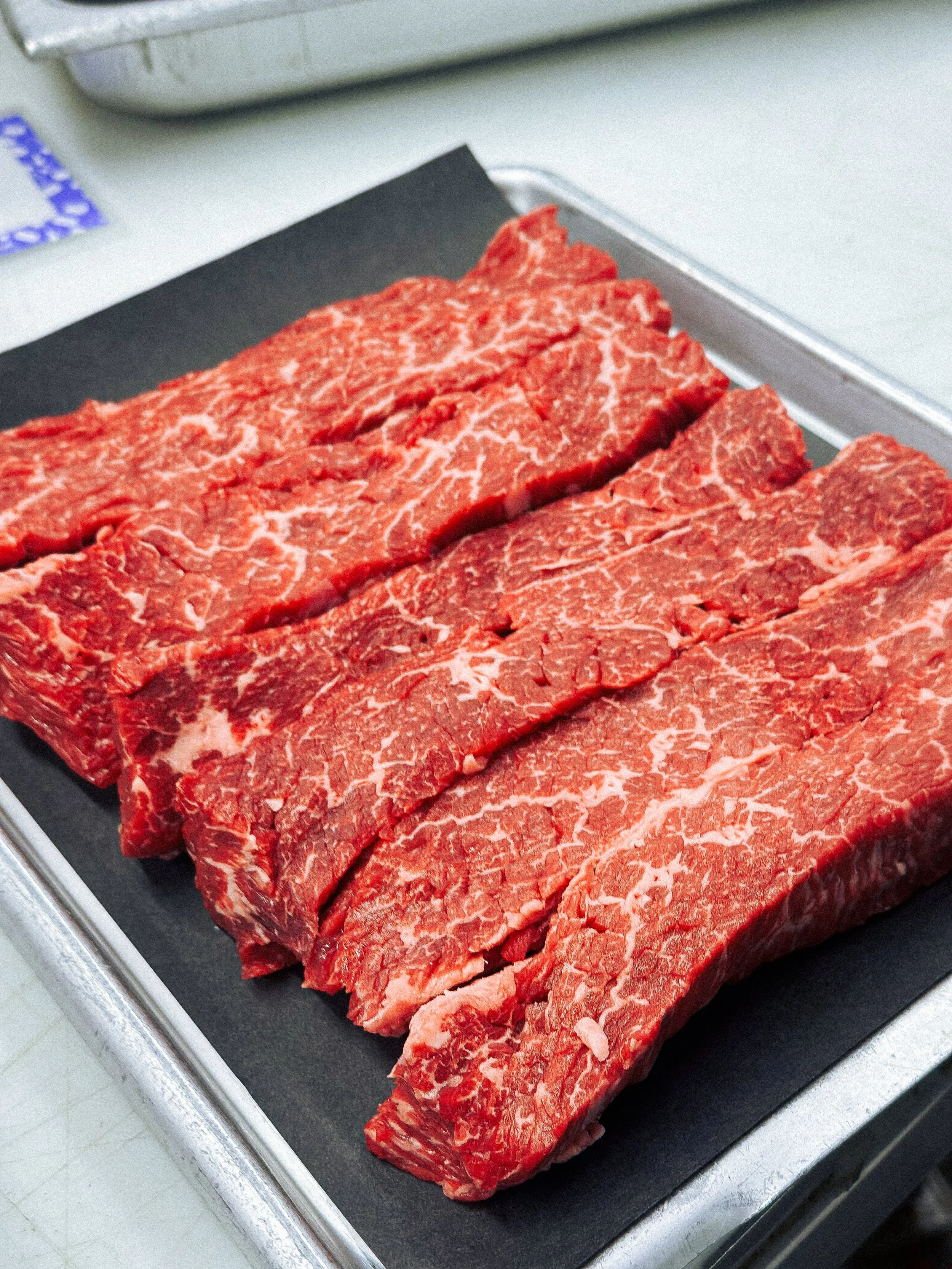 Three raw beef steaks with marbling on a black cutting board in a kitchen.