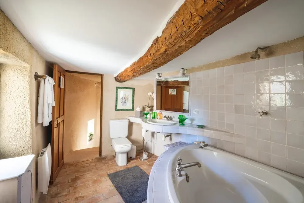 Salle de bain avec une baignoire, un miroir, un lavabo, un WC, et une étagère avec des décorations et des produits.