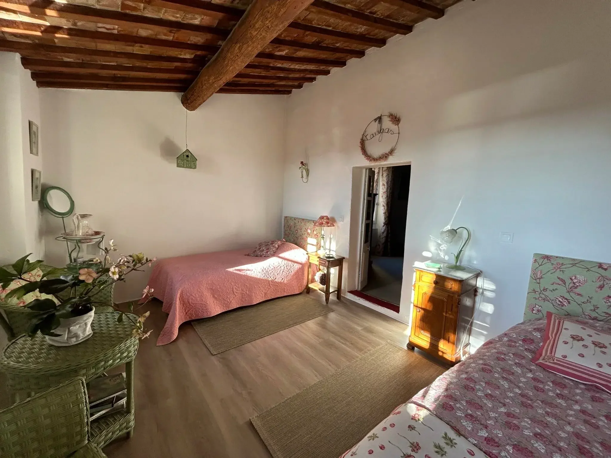 Une chambre confortable avec deux lits, décorée de fleurs, de mythes et de meubles en bois, avec des accents rustiques sur le plafond en bois.