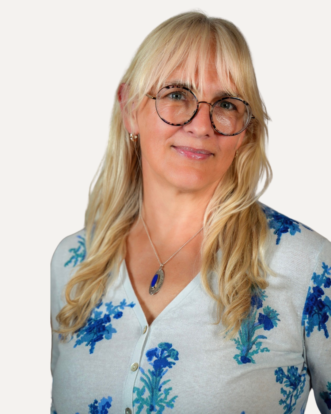 Picture of happy-looking therapist wearing a white shirt with blue flowers and smiling at the camera, wearing glasses.