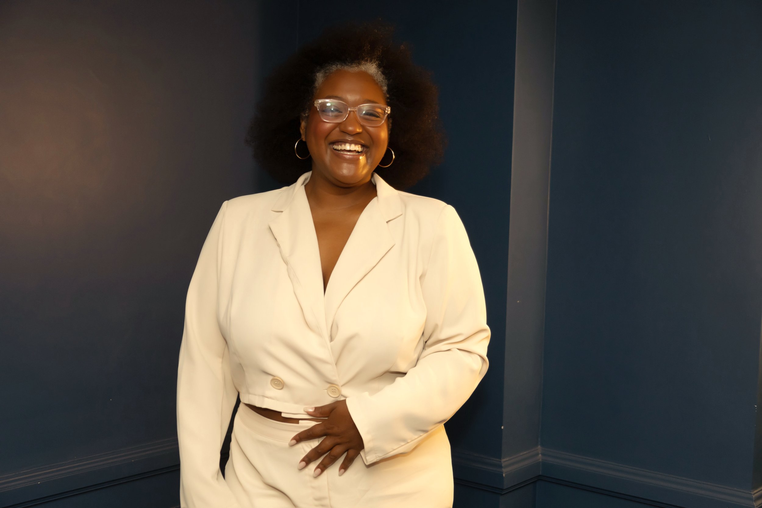Jenae Thompson, expert organic marketing consultant smiling, wearing a tailored cream suit and glasses against a deep blue background.