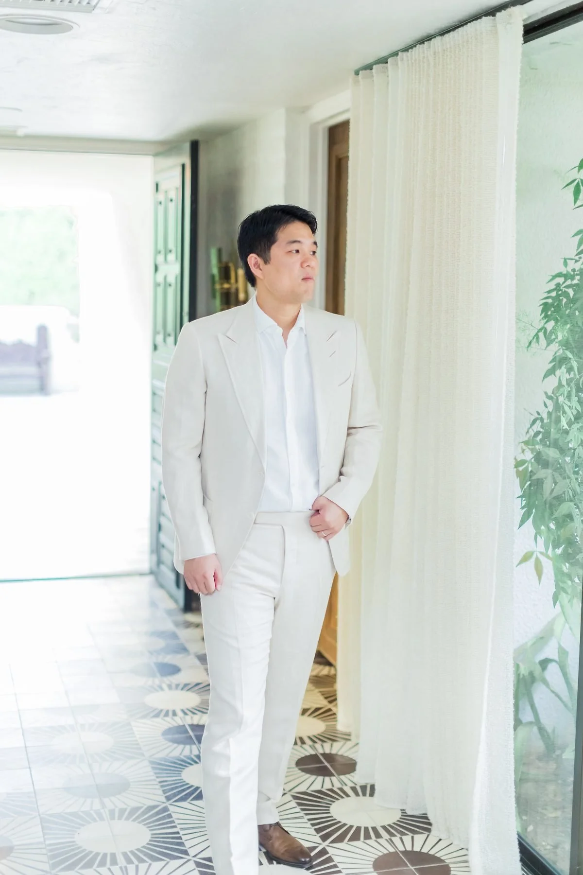Natalie's husband in a white suit, caught in a quiet candid moment by sheer curtains at the Palm Springs property.