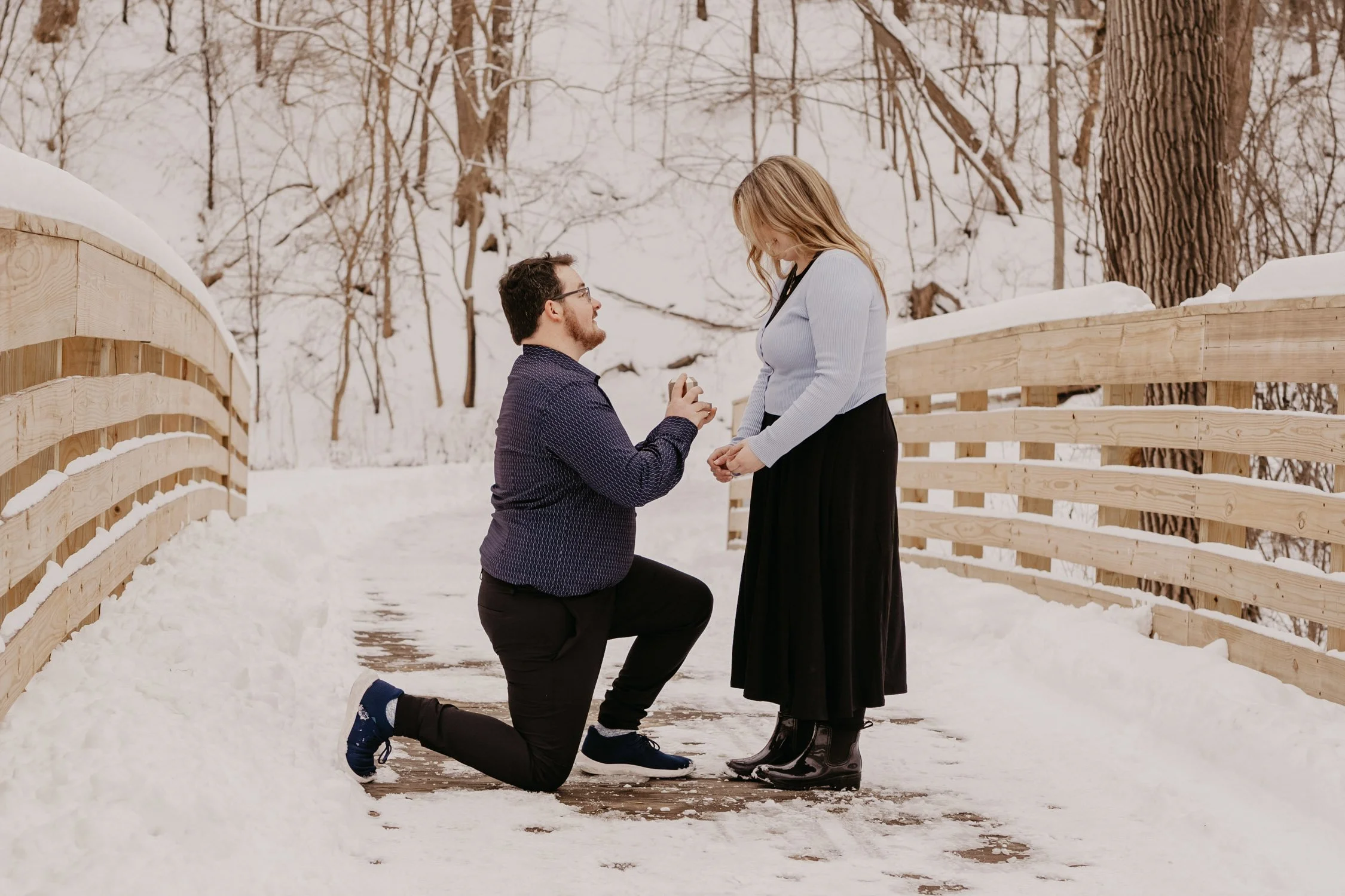 A man proposing on a snow covered bridge.