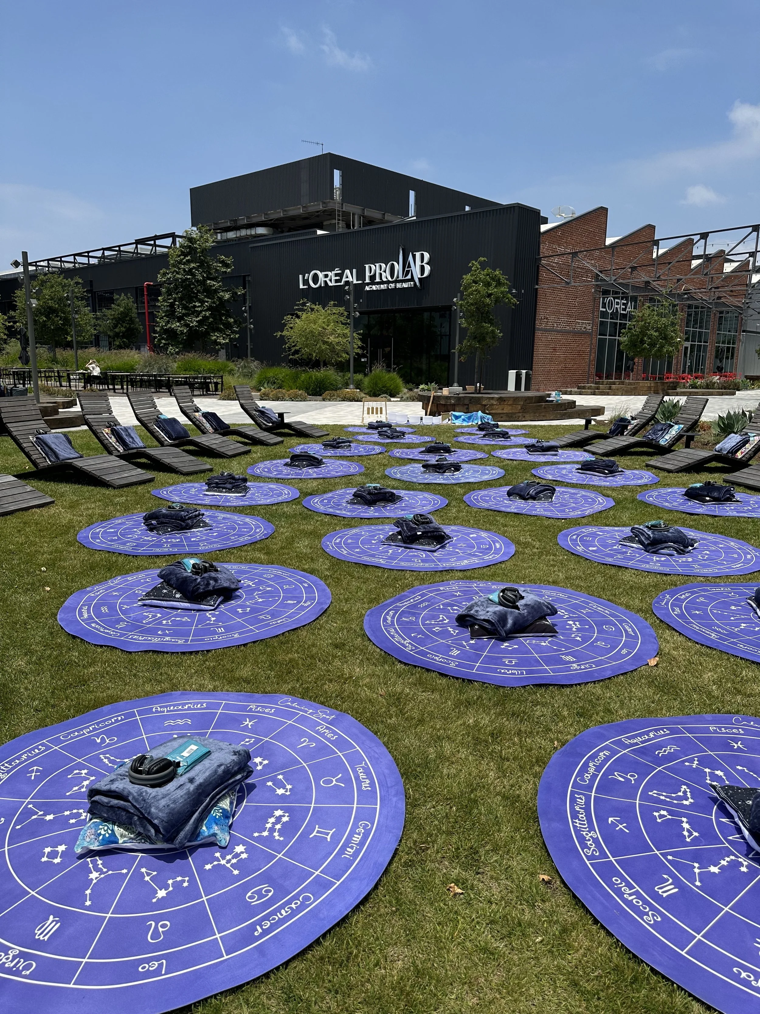 People participating in an outdoor yoga class on mats near a marina with sailboats, palm trees, and buildings in the background.