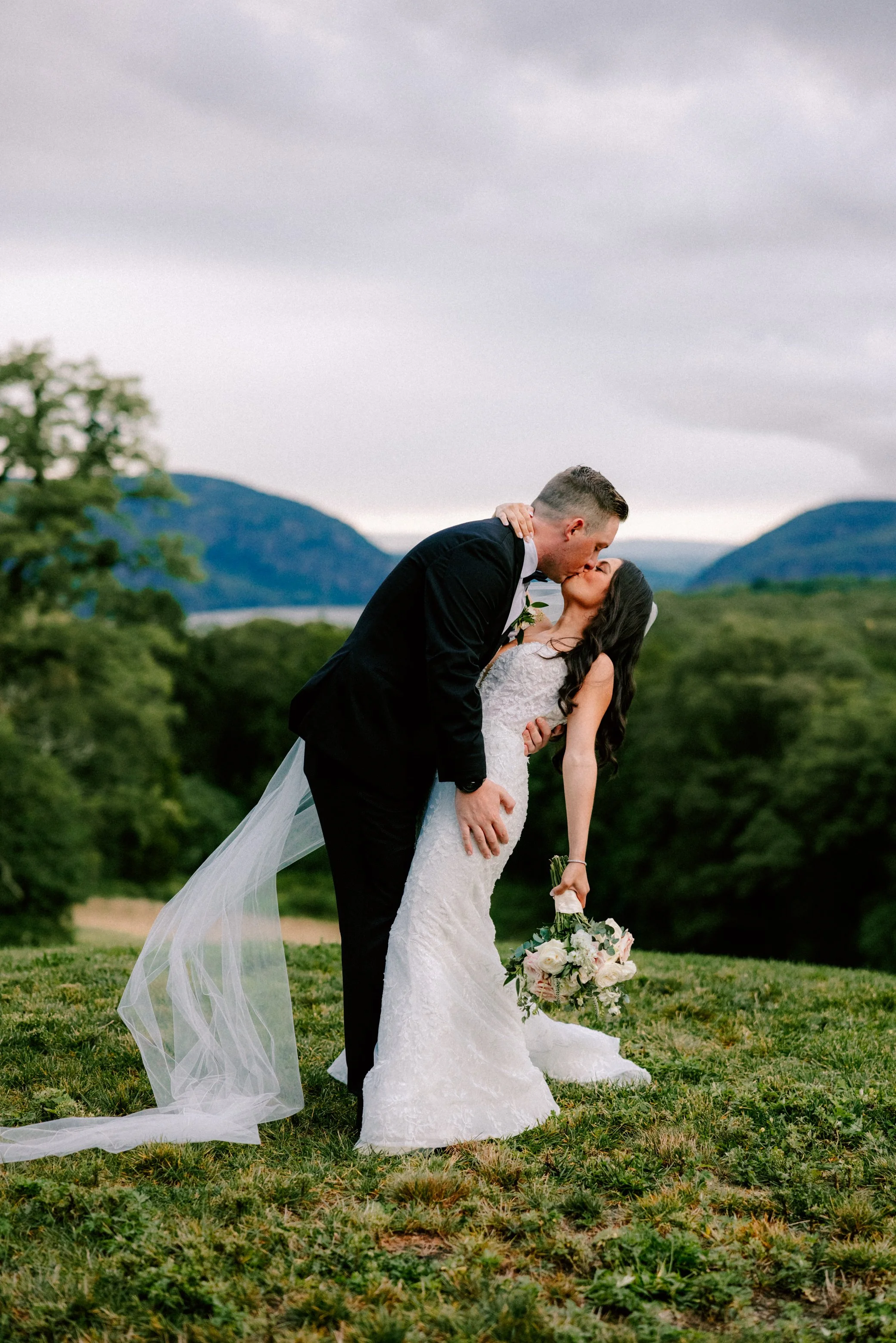 couple kiss in front of the view of the hudson river valley on their wedding day at the garrison