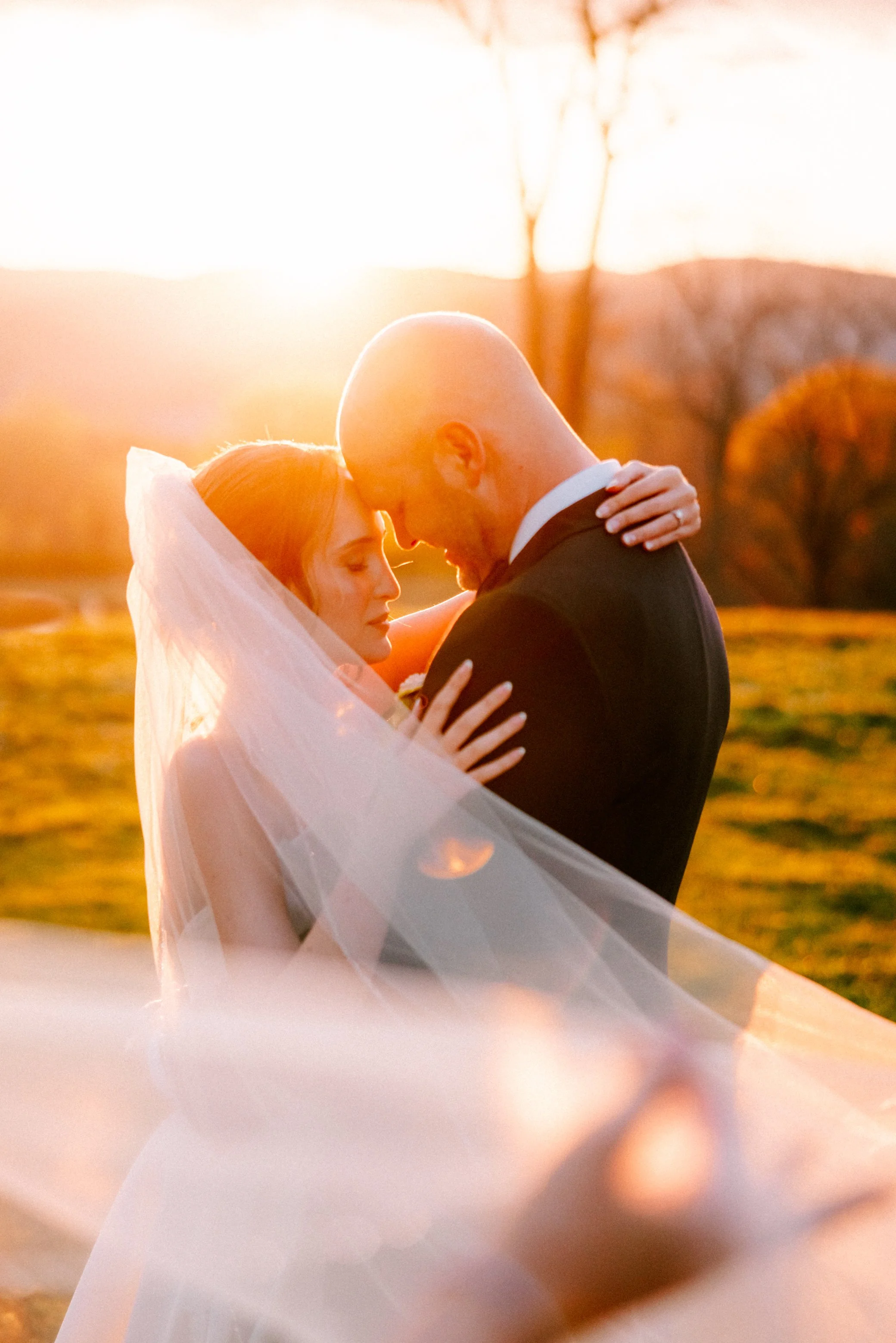 bride and groom resting their foreheads together with veil in the wind during golden hour at garrison new york