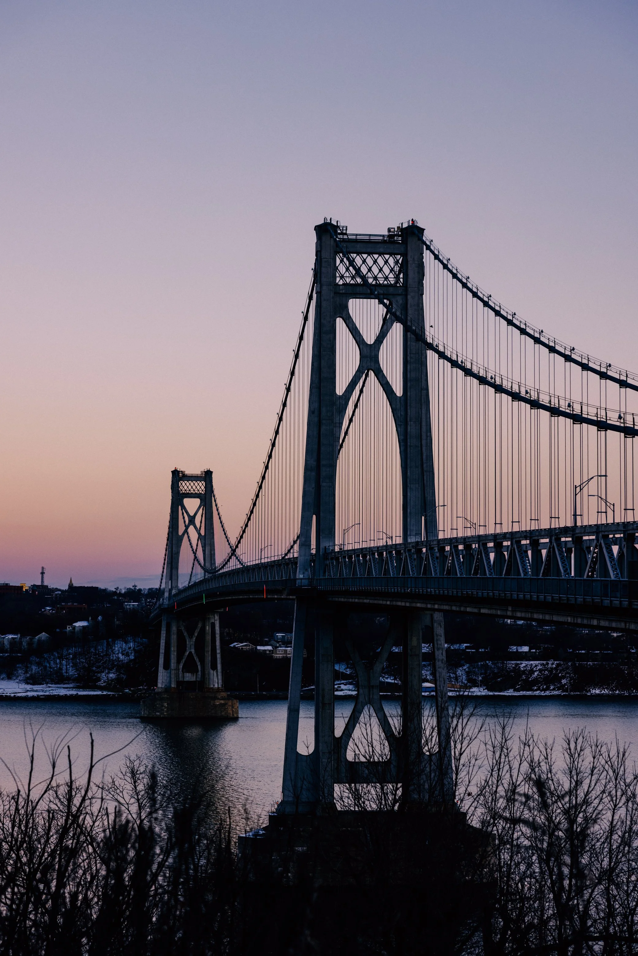 Photograph of The Mid-Hudson Bridge over a river at dusk, with a cityscape of Poughkeepsie, NY in the background by Caitlinn Mahar-Daniels, hudson valley wedding photographer.