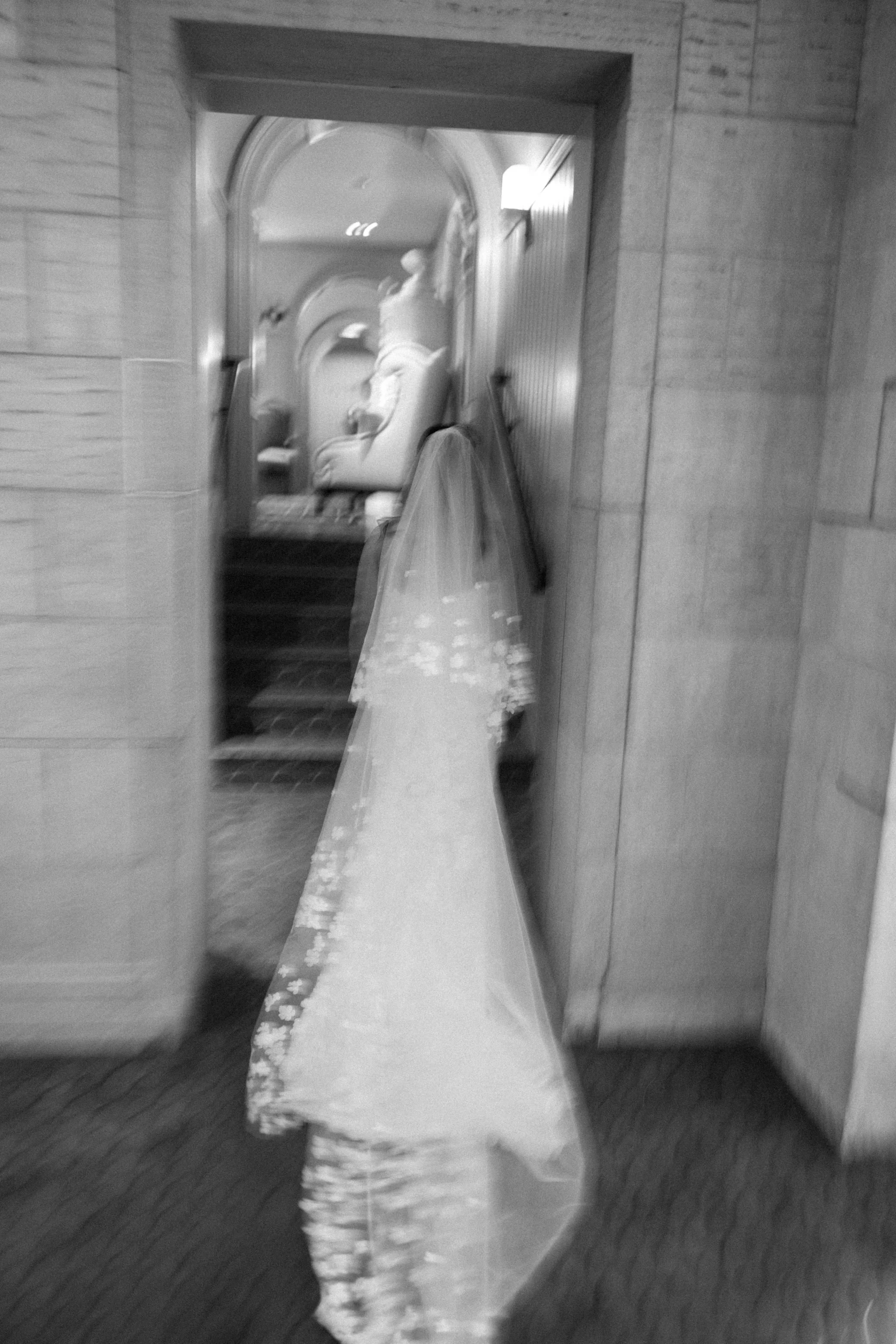 Blurry black and white photograph of bride quickly walking through Glenmere Mansion on her wedding day