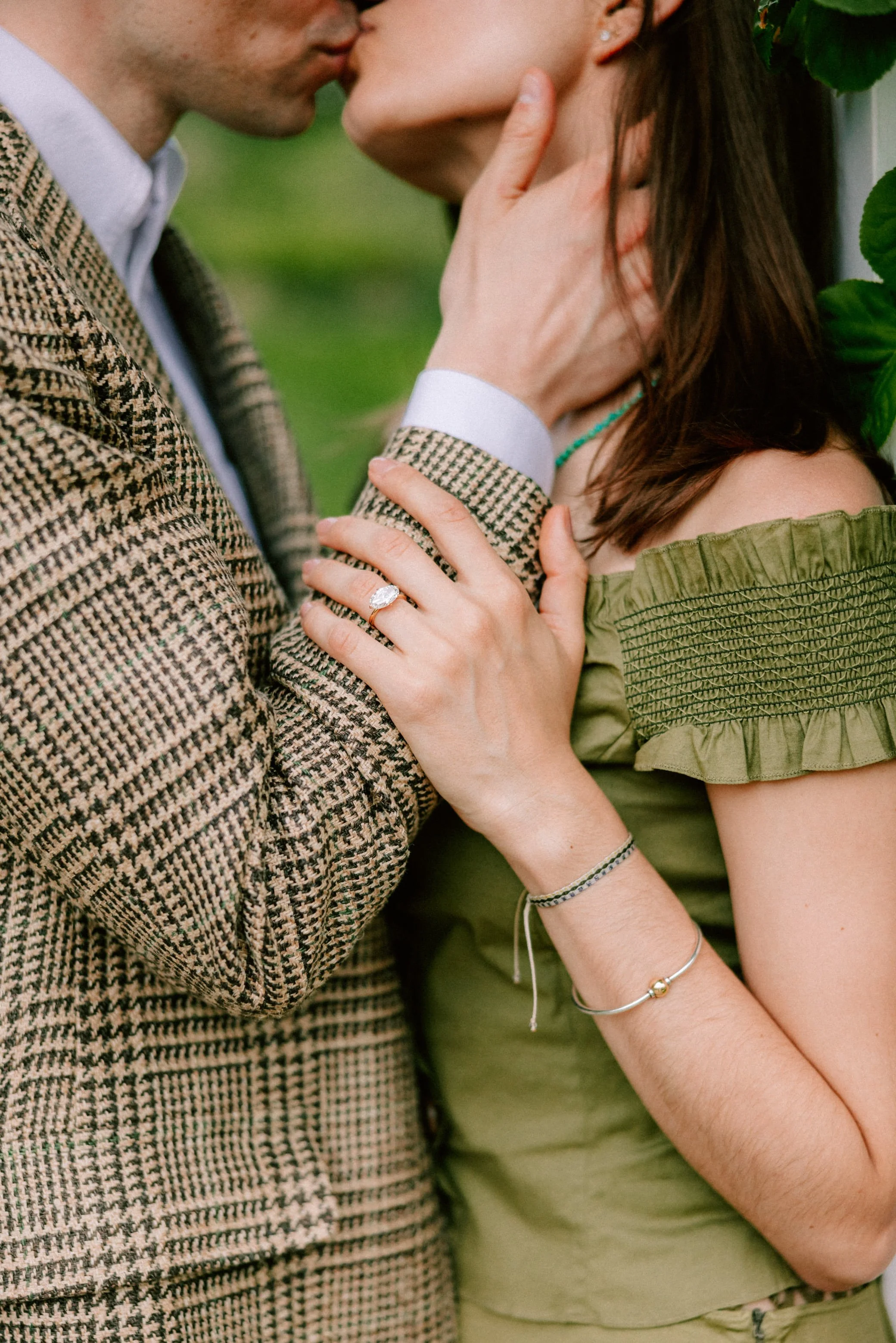 engaged couple kiss while man gently holds her neck and her hand rests of his arm with an engagement ring on her finger