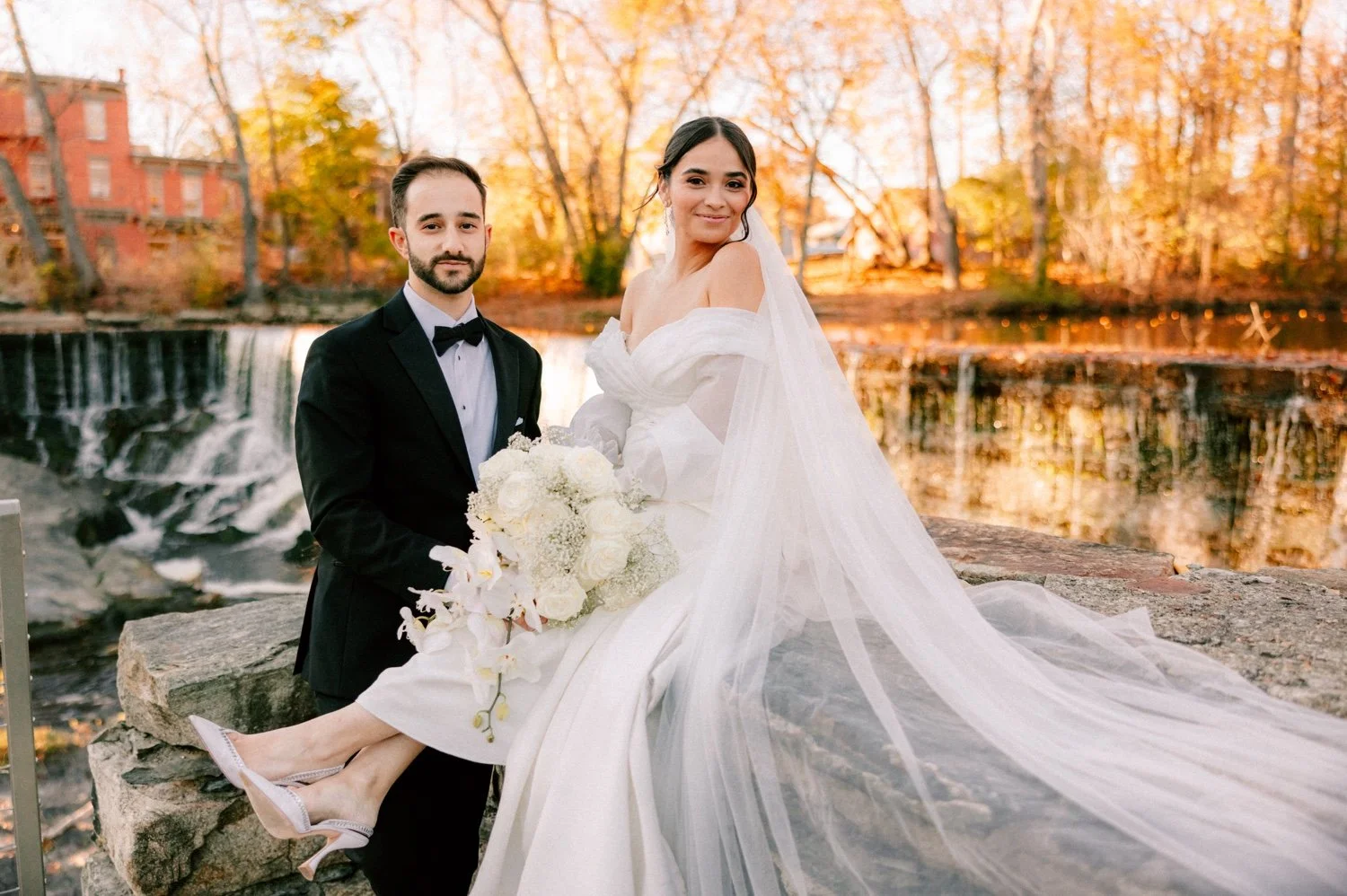 bride sitting while groom stands and looks into the camera in november at the roundhouse on their wedding day