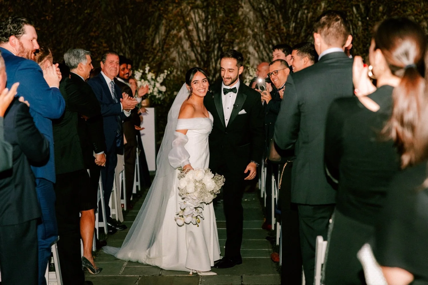 bride and groom walk down the aisle with flash photographs during their november wedding ceremony at the roundhouse