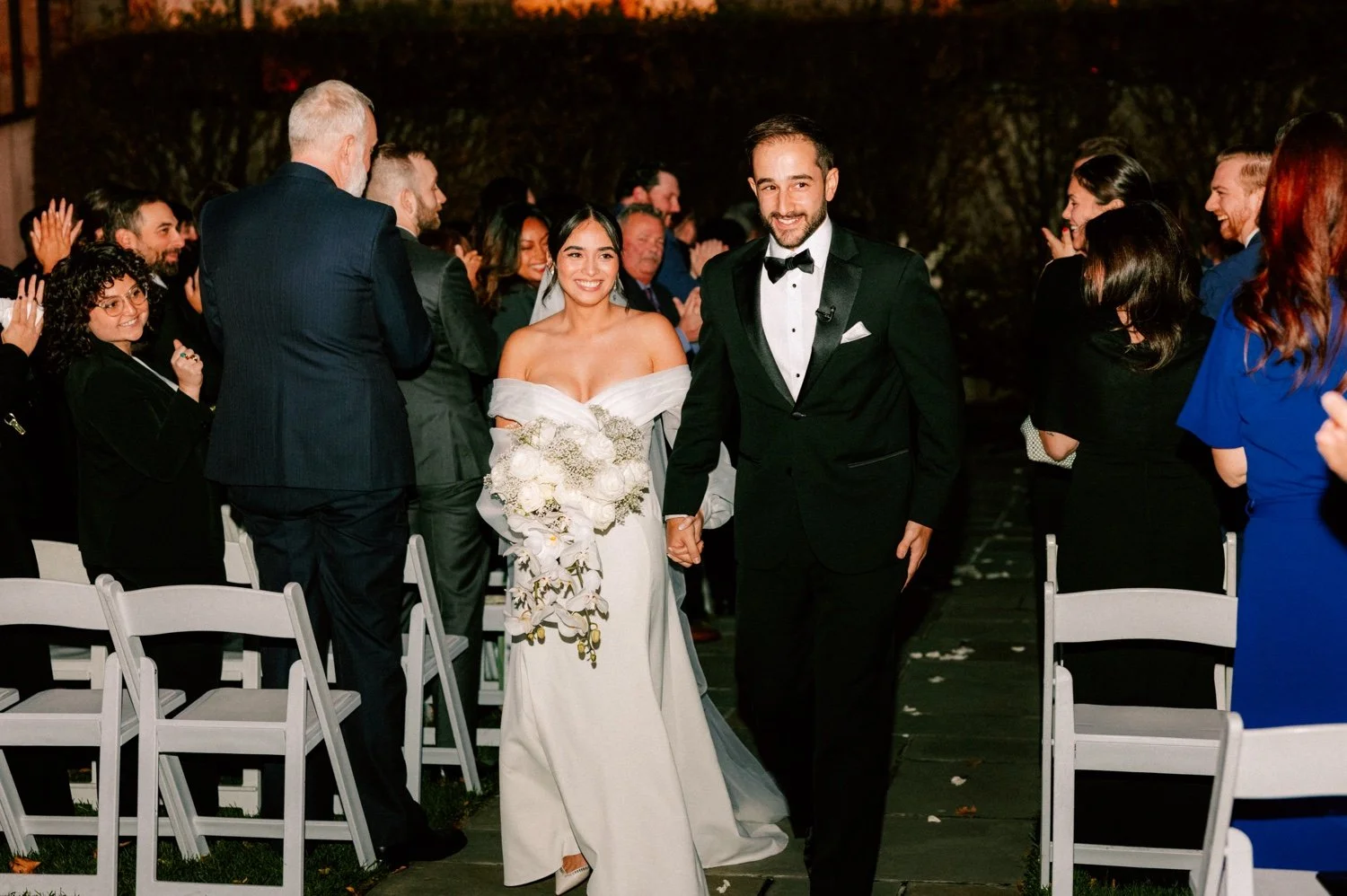 bride and groom walk down the aisle with flash photographs during their november wedding ceremony at the roundhouse
