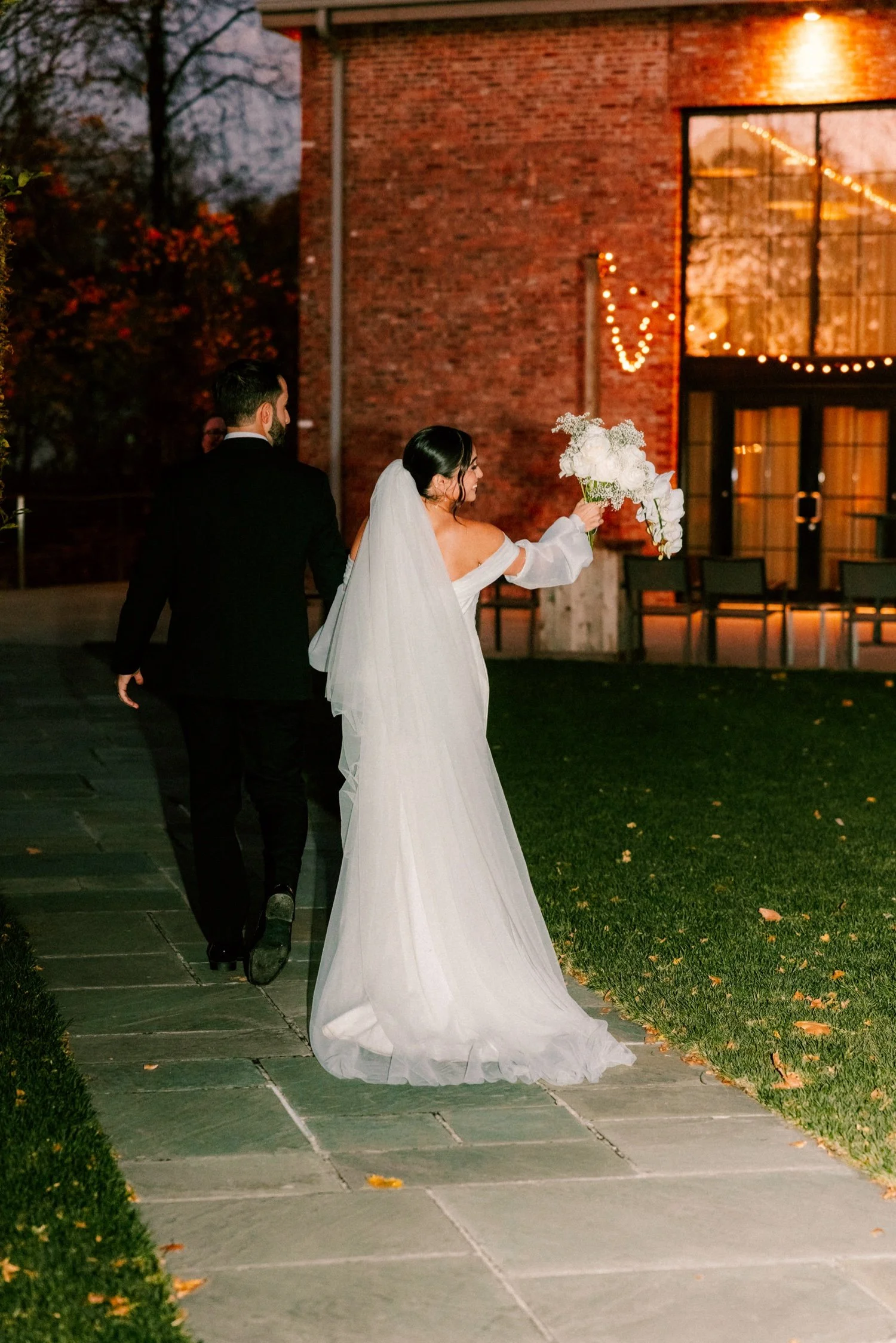 bride holds up bouquet as her and groom walk down aisle in the dark during outdoor autumn wedding ceremony at the roundhouse