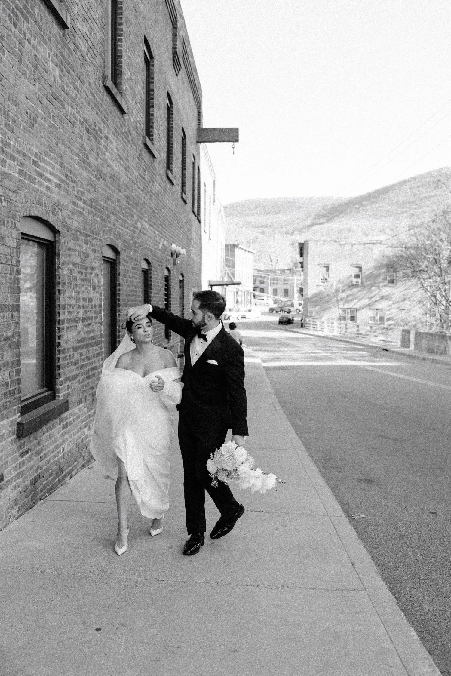 documentary black and white photograph of groom moving brides hair out of her face while walking down the street on their wedding day at the roundhouse