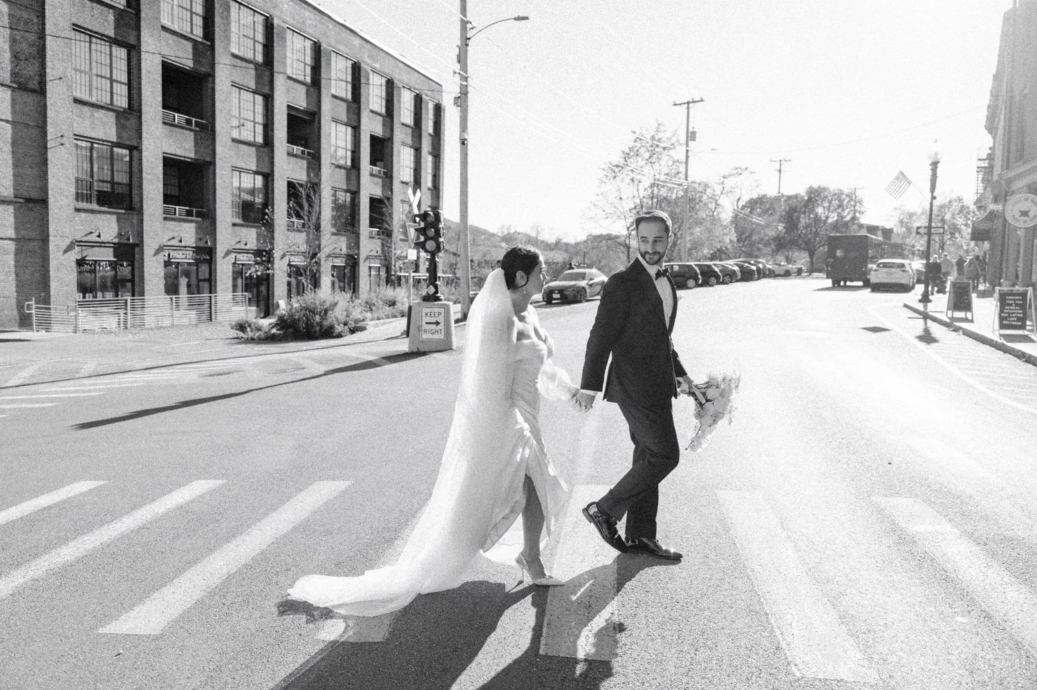 documentary black and white photograph of wedding couple walking in the sunshine across the street in beacon ny at the roundhouse