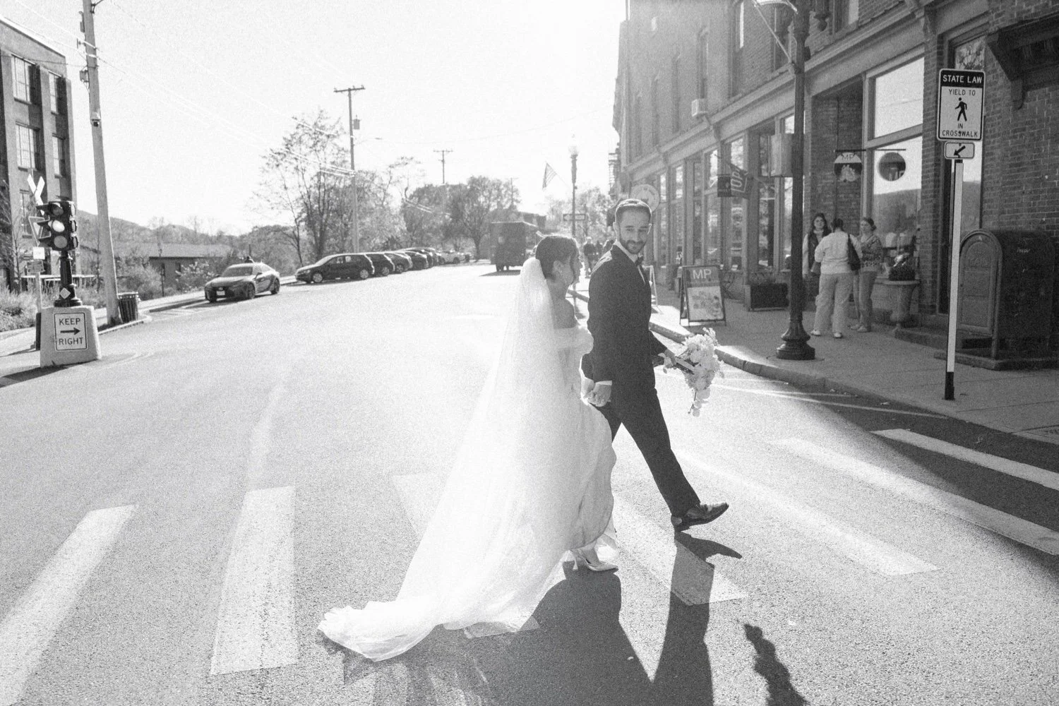 documentary black and white photograph of wedding couple walking in the sunshine across the street in beacon ny at the roundhouse