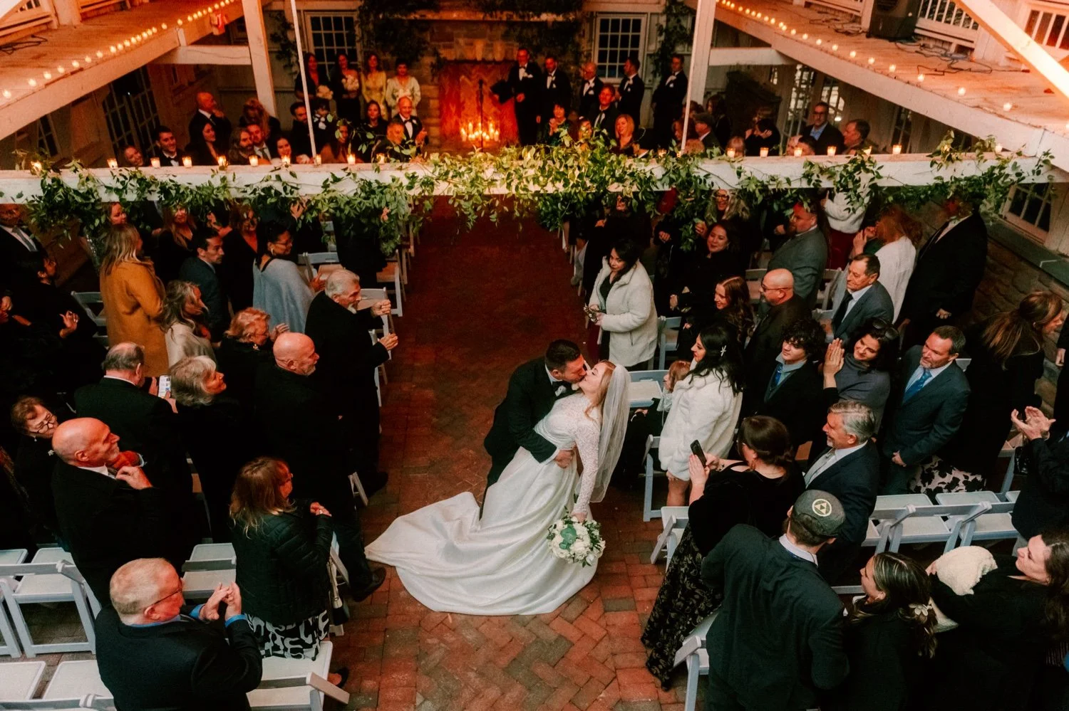 groom dips and kisses bride in the middle of the aisle during their indoor winter wedding ceremony at the ashford estate
