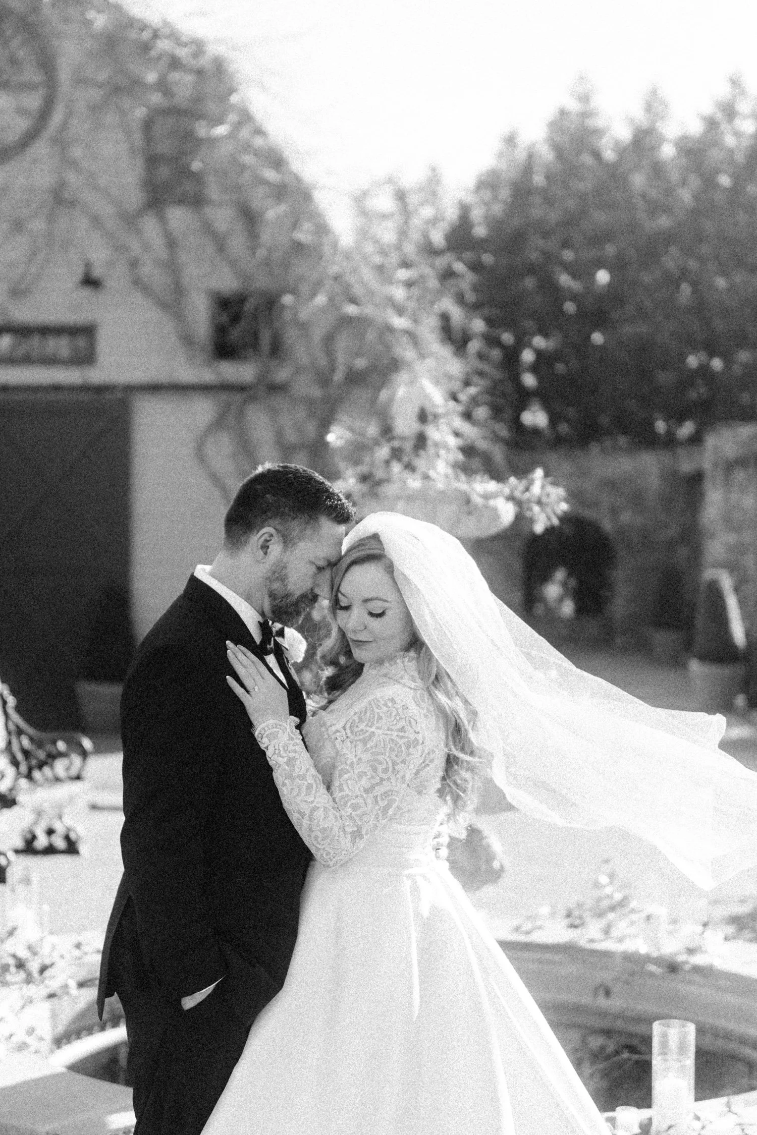 classic black and white portrait of wedding couple with bride’s veil in front of barn