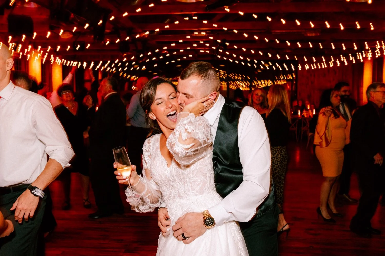  groom embraces bride from behind and kisses her on the cheek while she holds a glass of champagne on the dancefloor at city winery hudson valley 