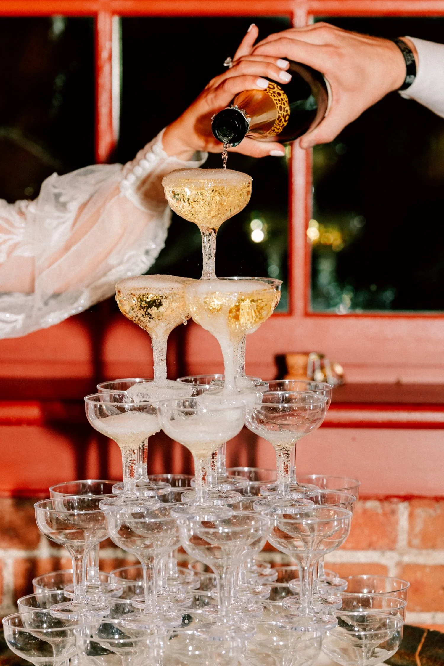  bride and groom hold bottle together as they pour wine over their champagne tower at city winery hudson valley 