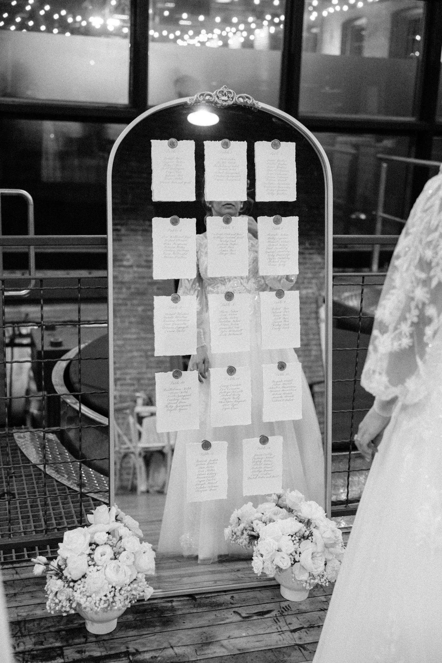  black and white photo of mirror seating chart while bride looks at it inside city winery hudson valley 