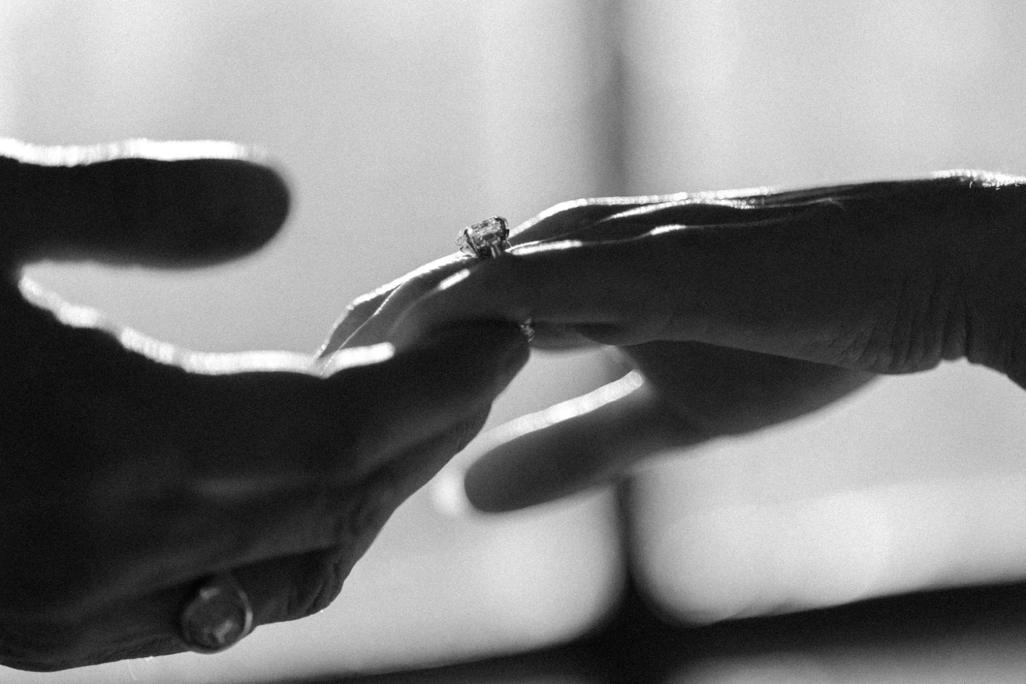  black and white photo of hands reaching for one another with engagement ring at brunette wine bar 