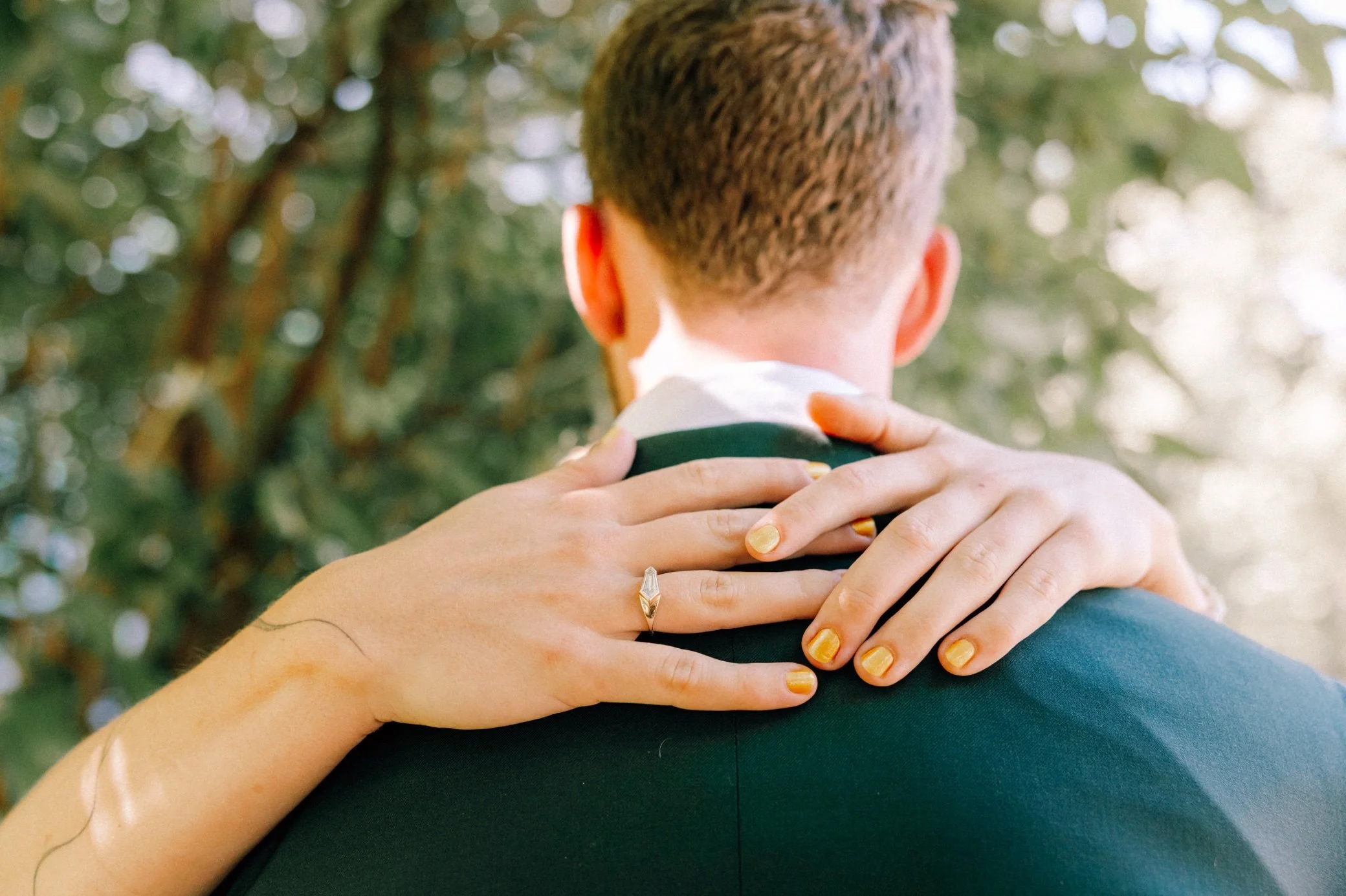  bride’s hands with gold nail polish around grooms shoulders 