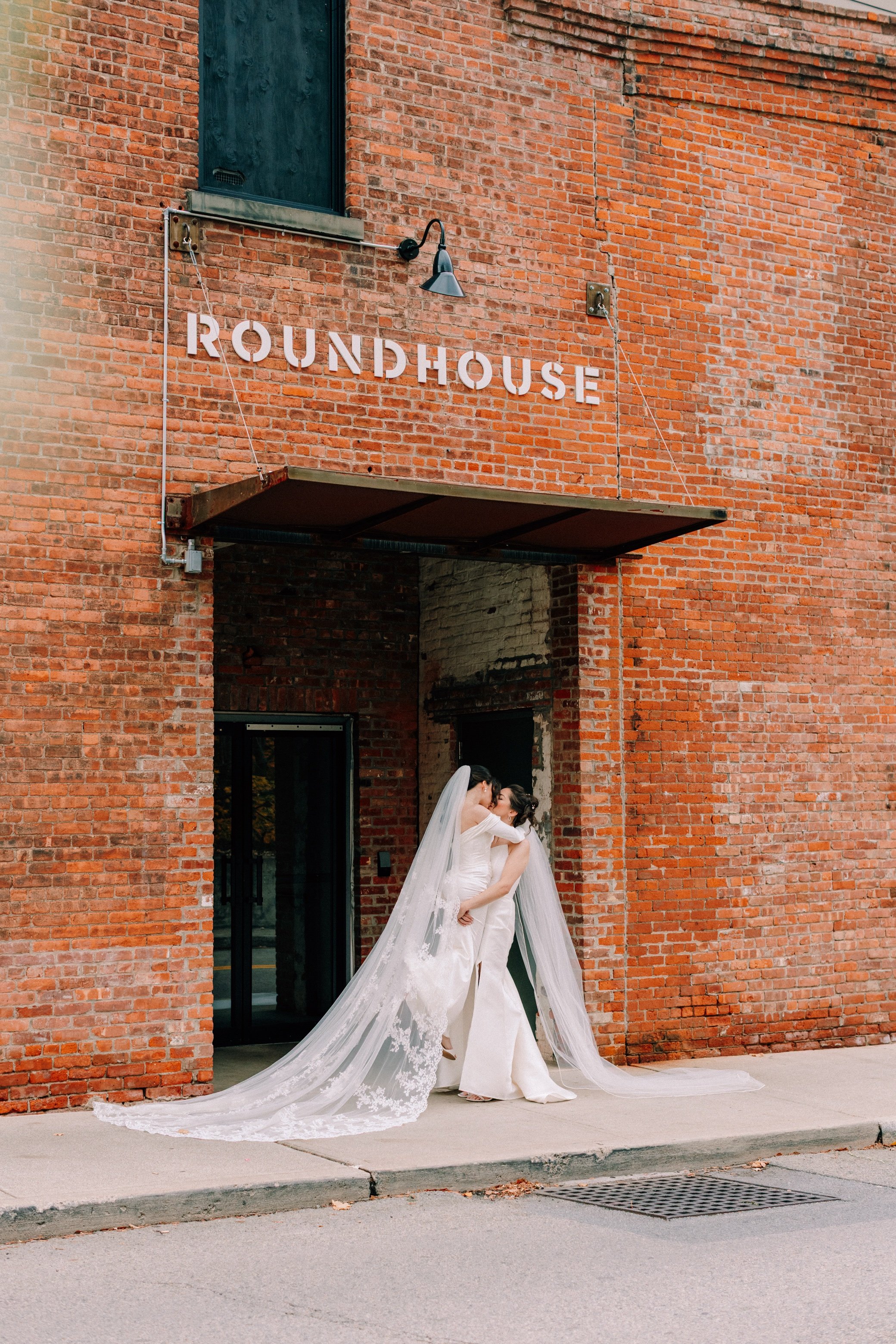  bride lifts bride with veils falling behind in front of The Roundhouse in Beacon, NY 