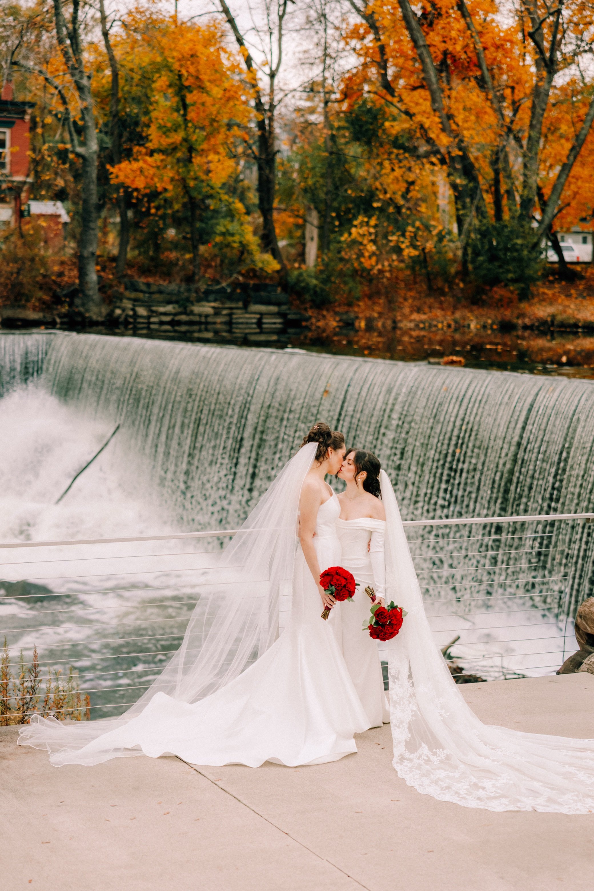  brides kissing while holding red bouquets in front of beacon falls at the roundhouse  