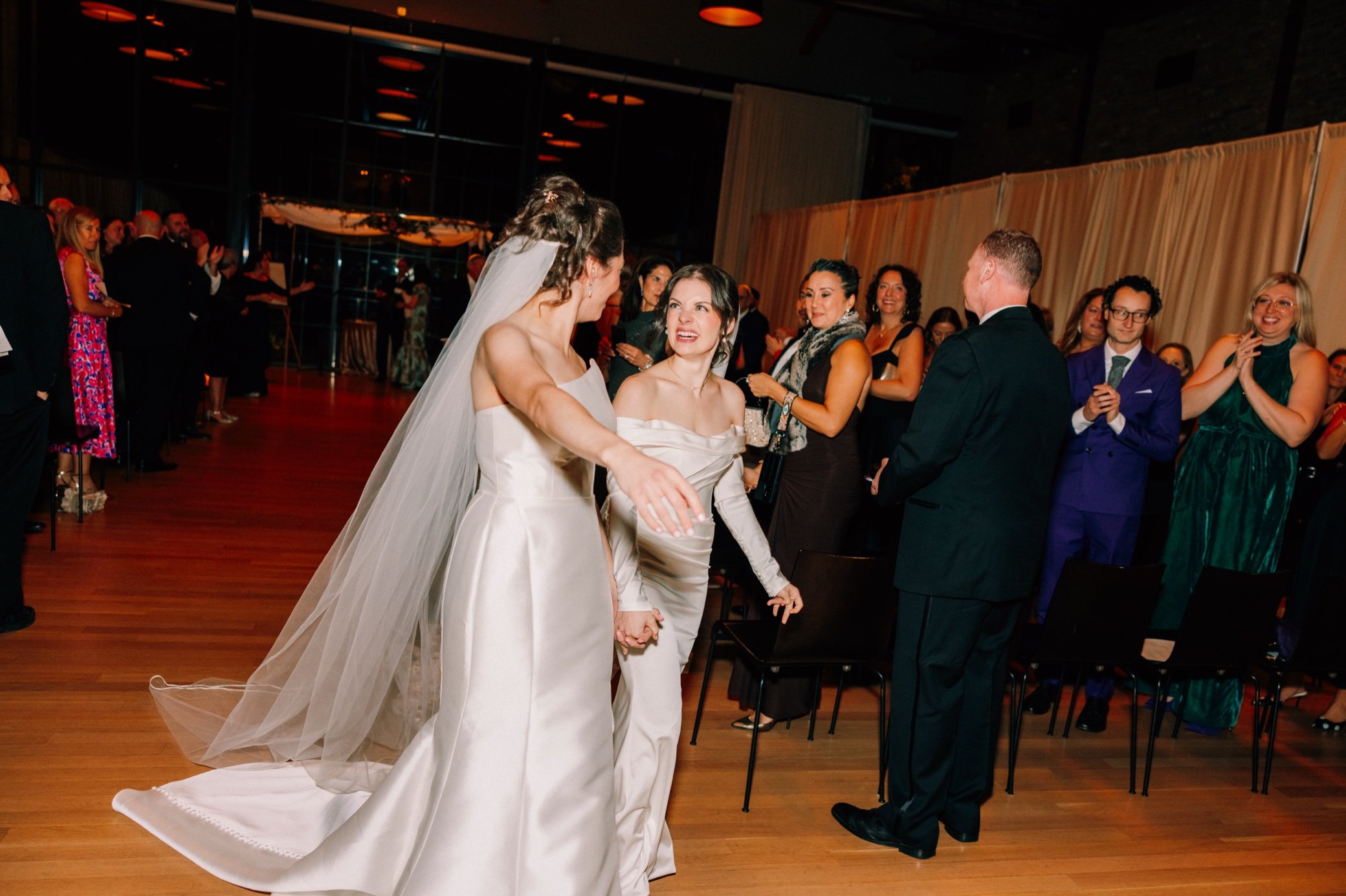  brides holding hands and walk down aisle at the roundhouse 